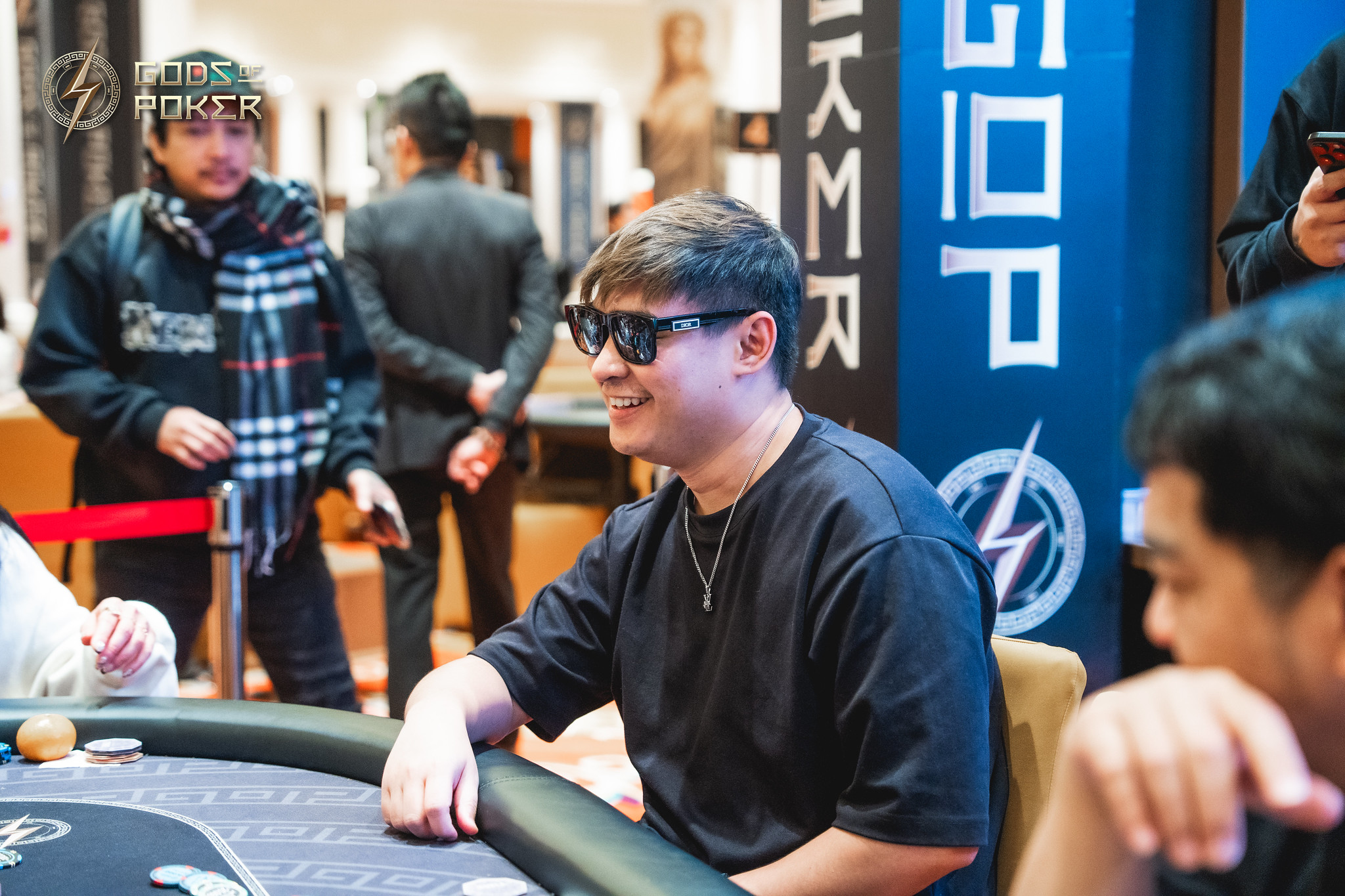 Man in sunglasses smiles while playing poker at a table.