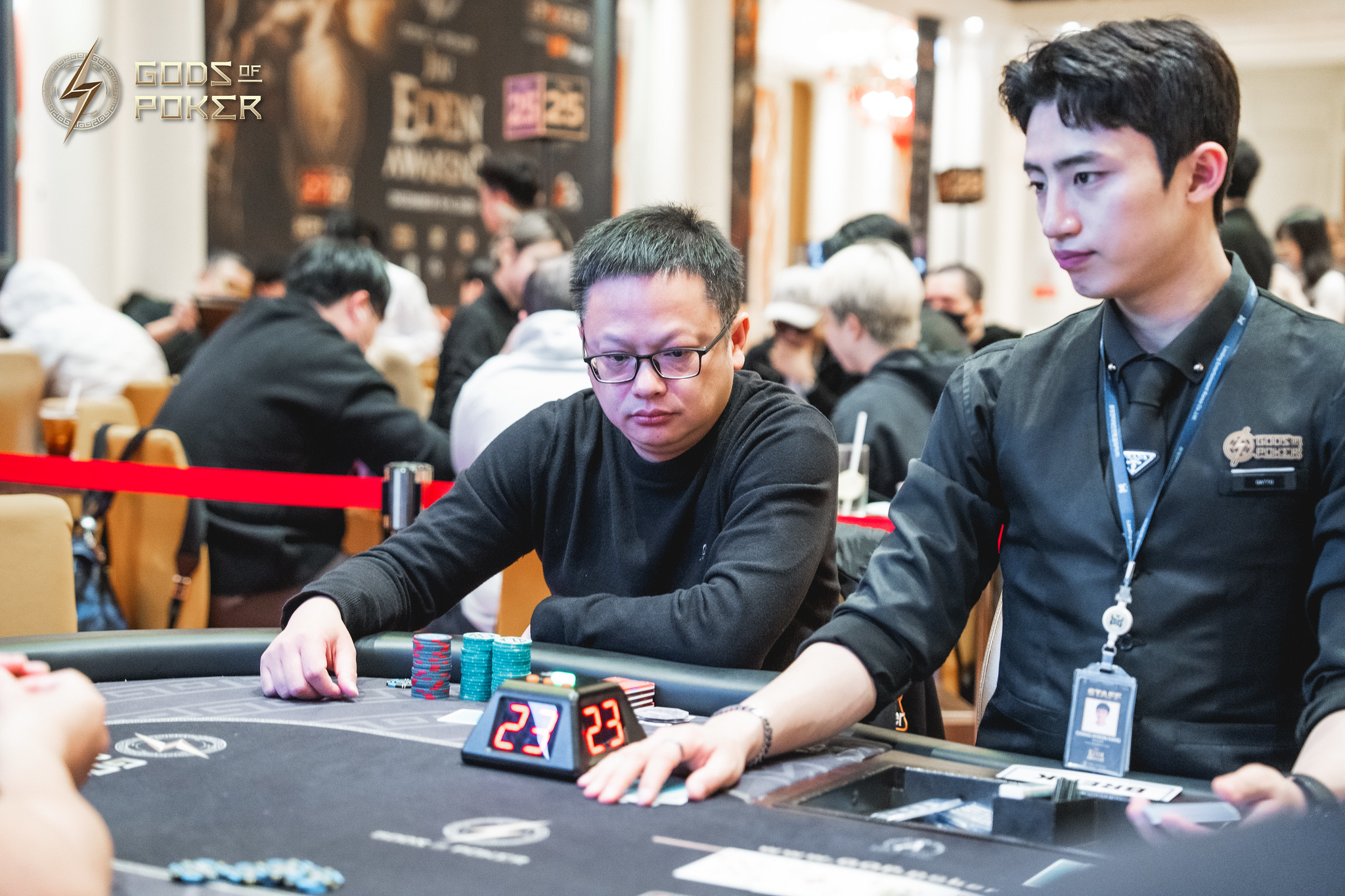 Two men focused on their hands at a poker table with chips and a timer.