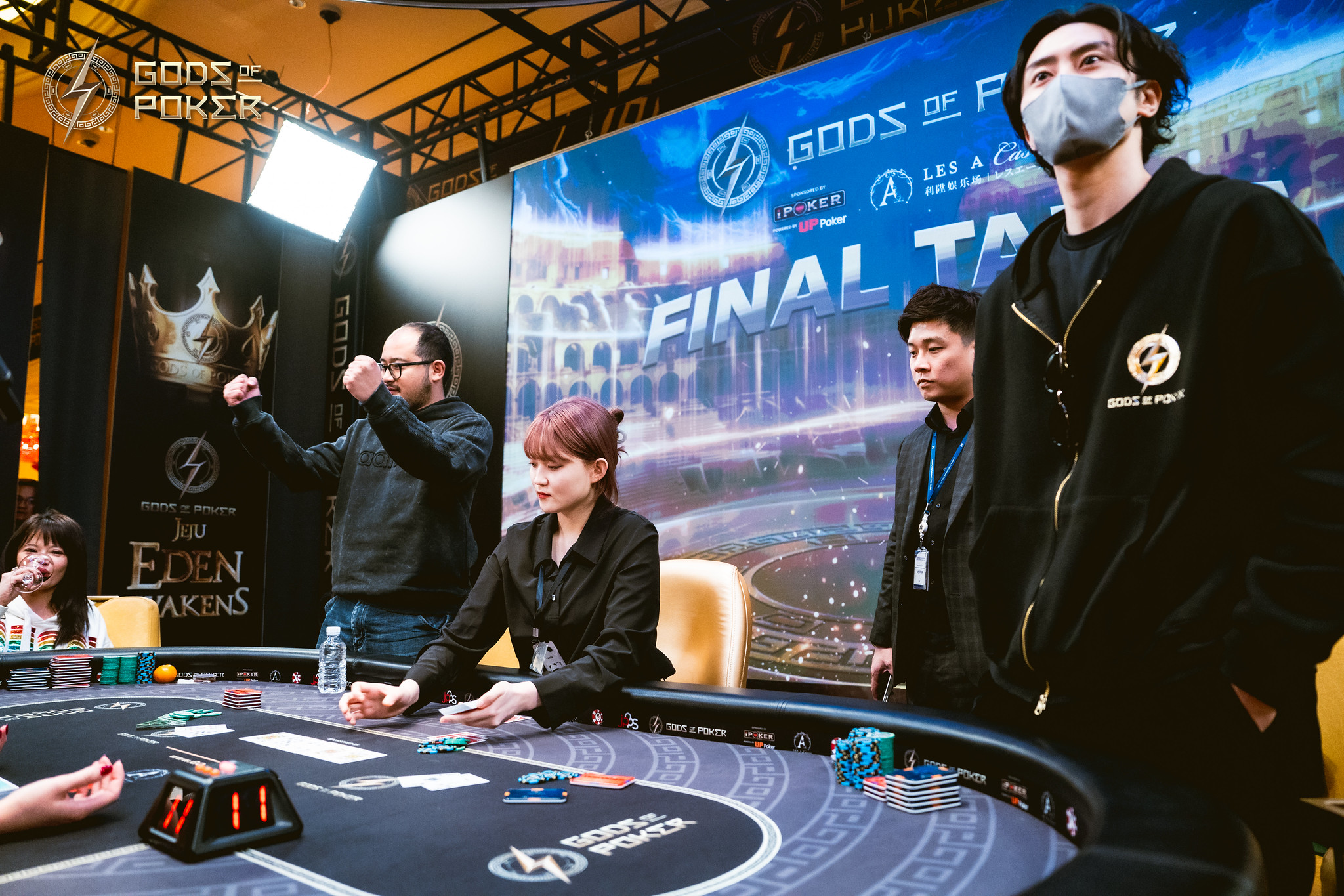 Players at a poker tournament table, with one man celebrating and another observing.