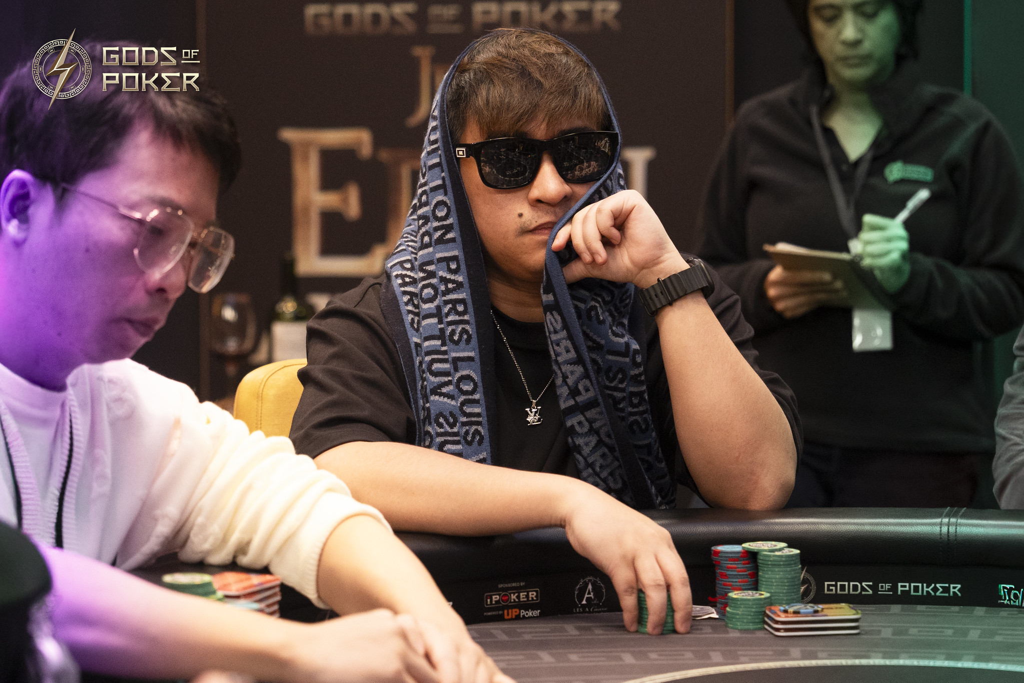 Man in sunglasses and patterned scarf plays poker, with chips on the table.