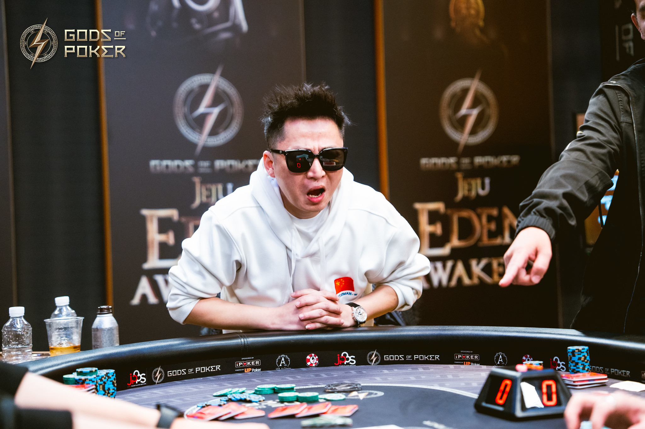 Man in sunglasses and white hoodie reacting intensely at a poker table.