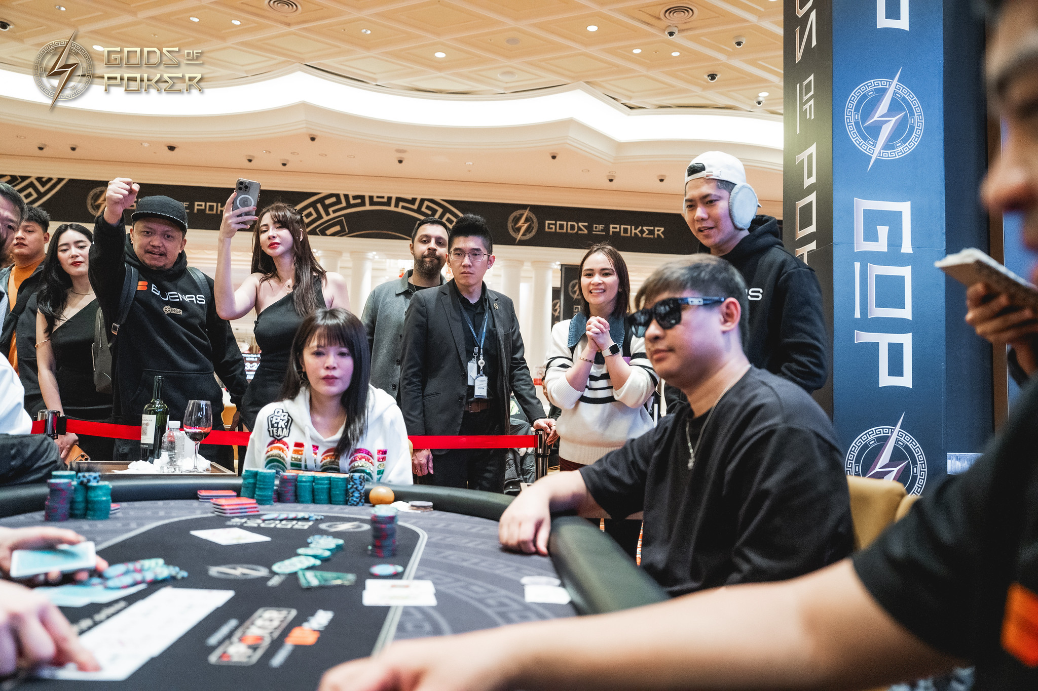 A poker player sits at a table with spectators watching a tense game.