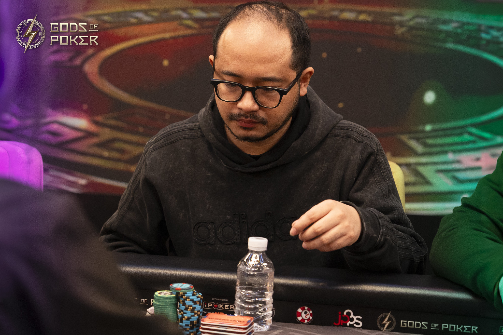 A man with glasses concentrates on a poker game, with chips and a water bottle.