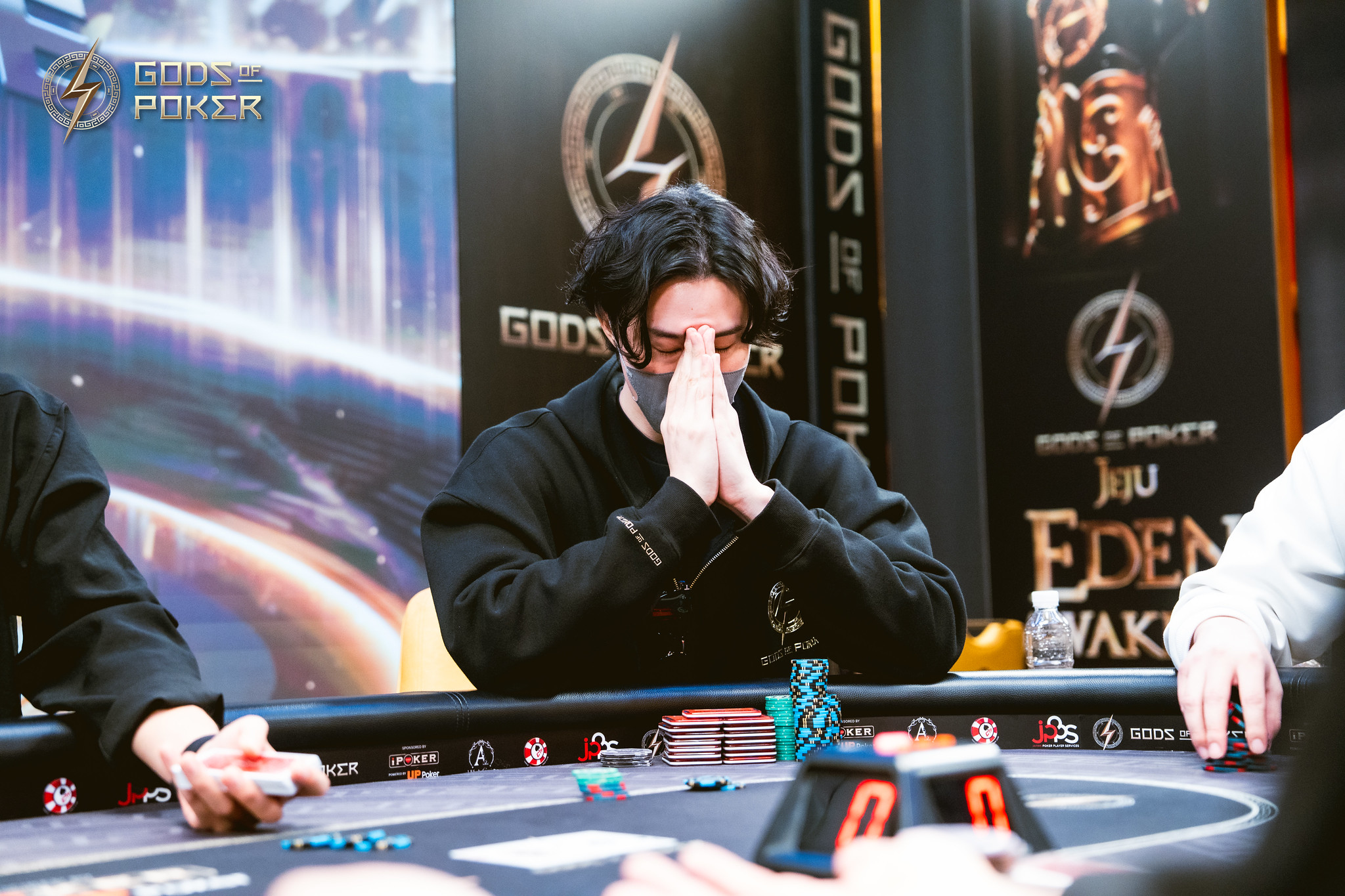A man at a poker table with clasped hands covering his face in intense concentration.