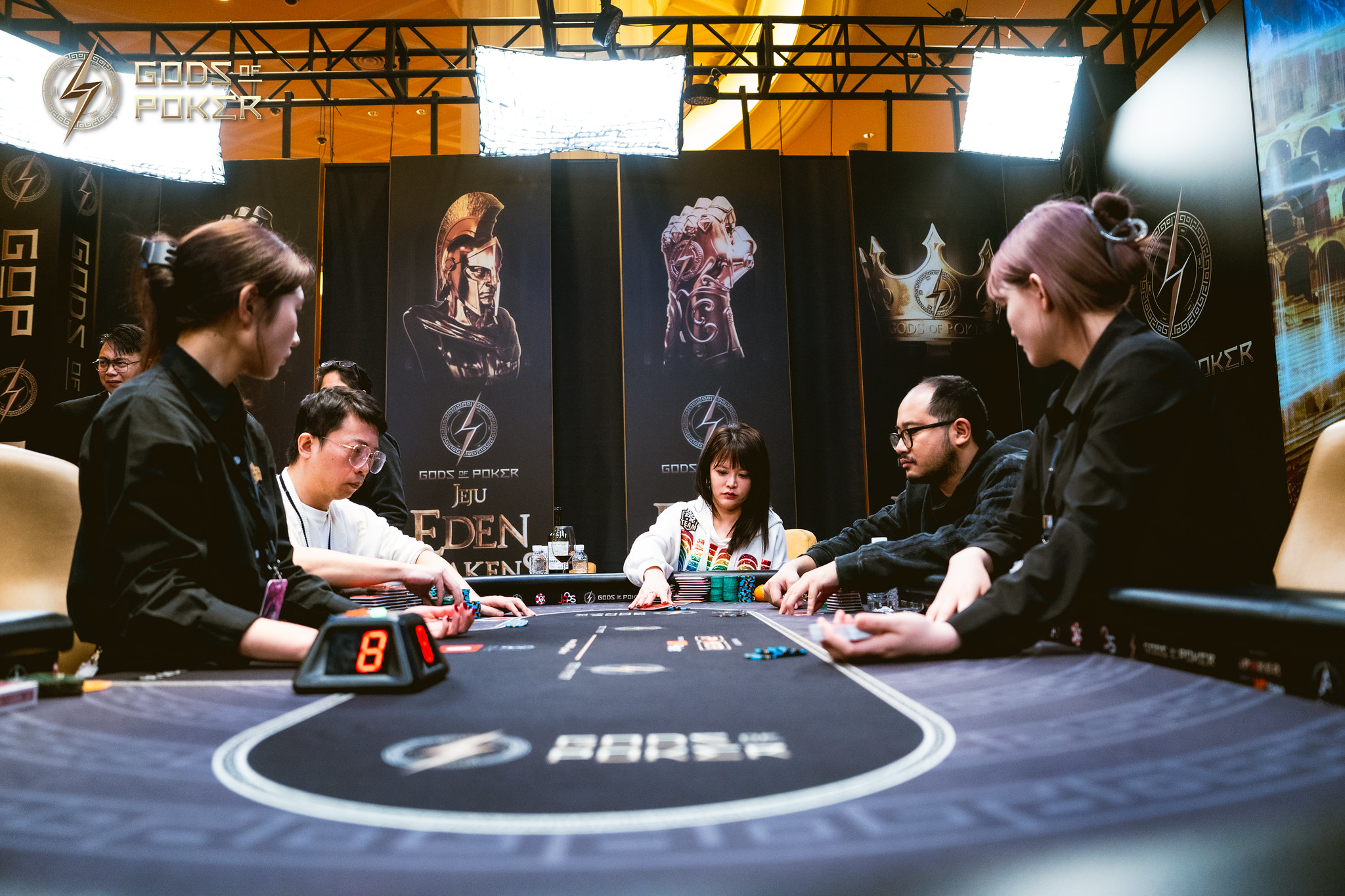 Poker players focused during a tournament at a branded table with cards and chips.