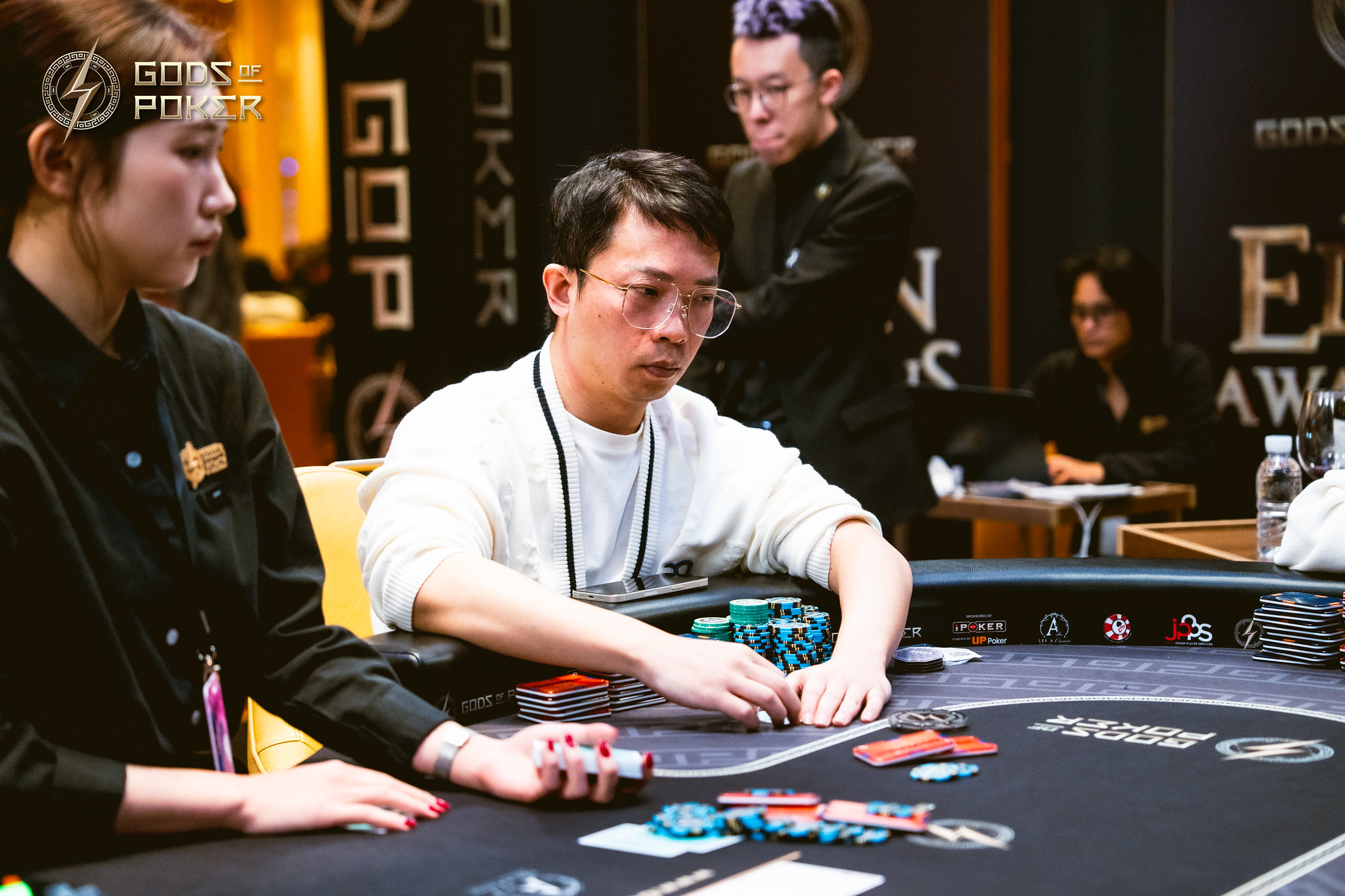 A man in glasses plays poker, focusing on chips and cards at a professional table.