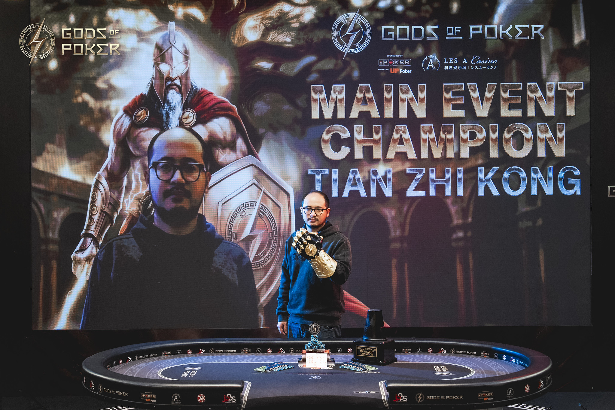 Tian Zhi Kong stands on stage celebrating his Gods of Poker Main Event Championship victory.
