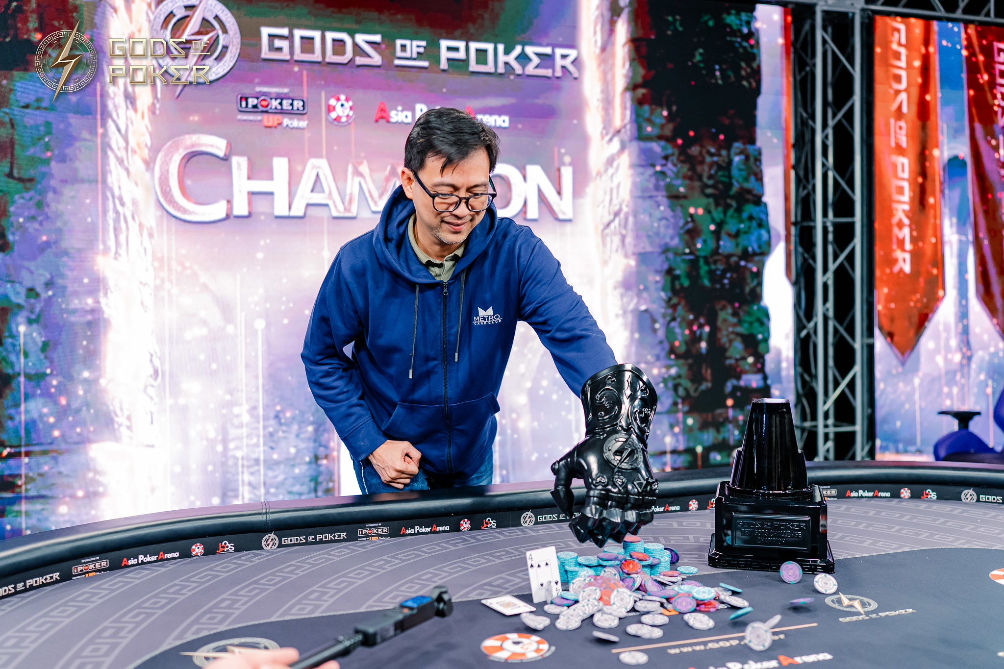 Smiling poker player celebrates his victory at a table with chips and a unique trophy.