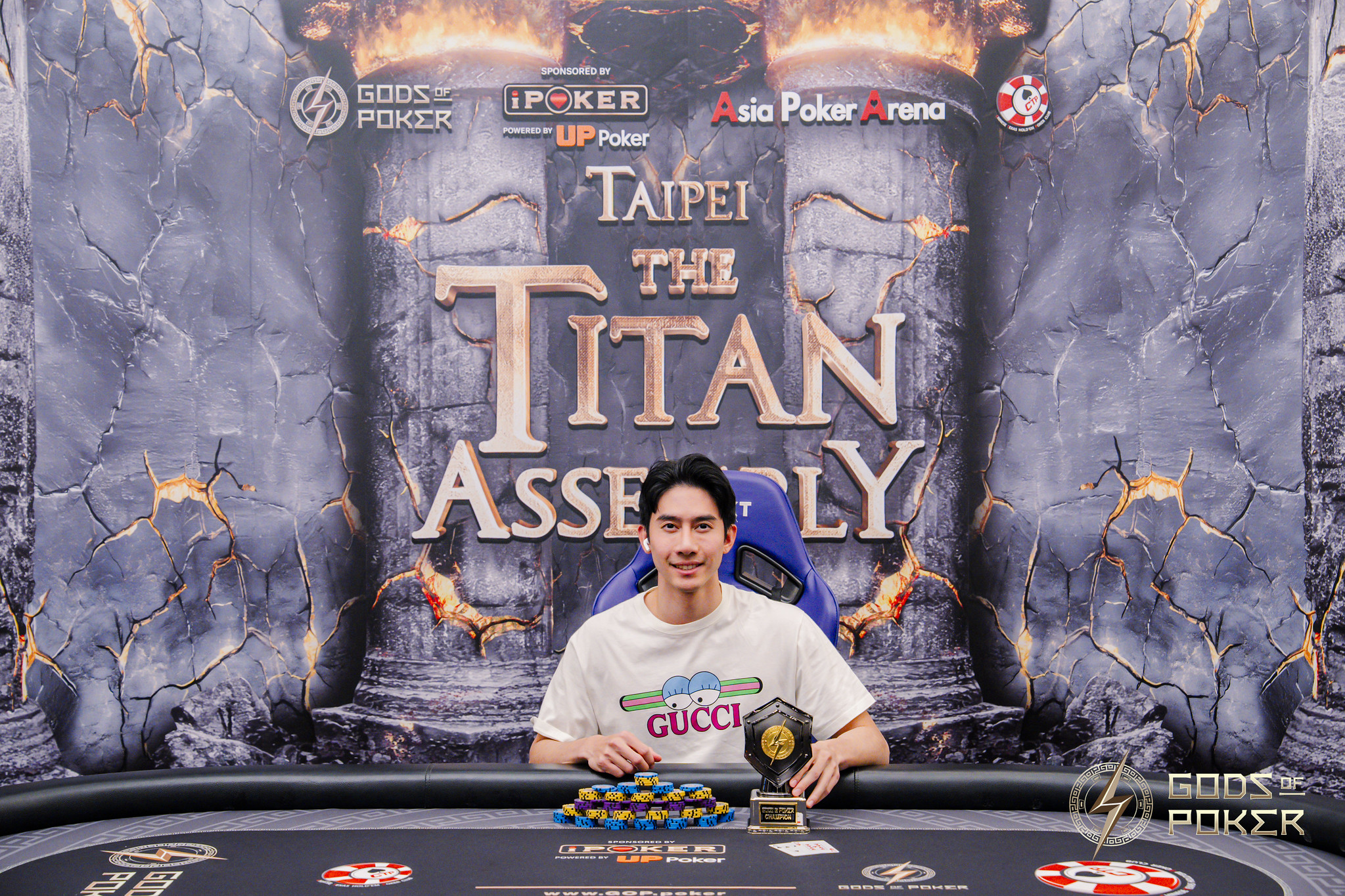 Smiling man at poker table with trophy and chips for 'TAIPEI THE TITAN ASSEMBLY' event.