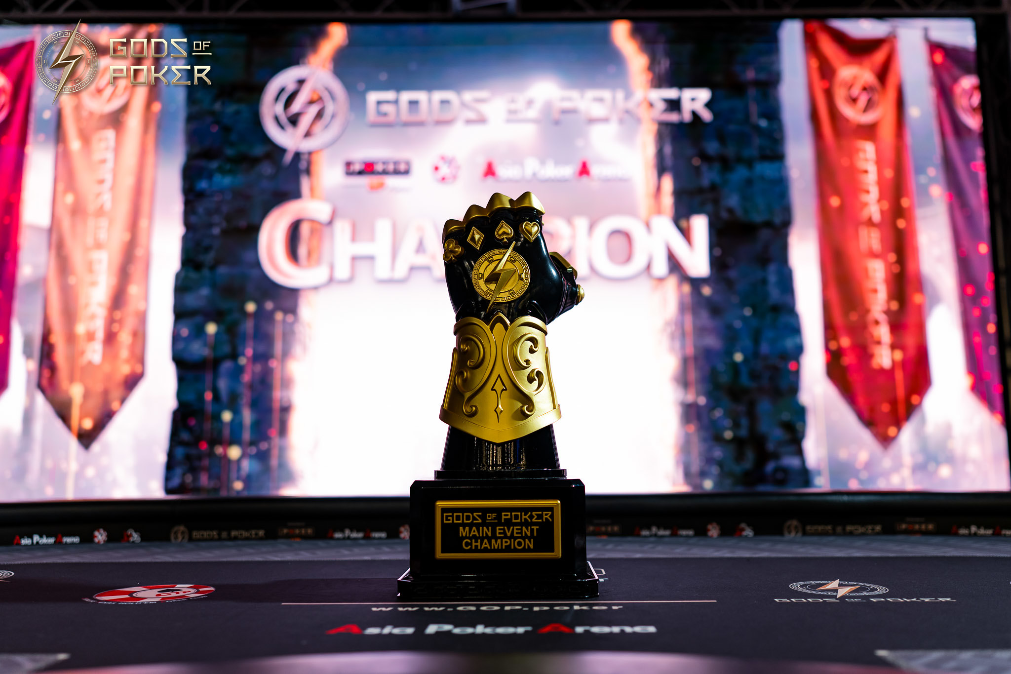Golden gauntlet-shaped trophy stands on a stage before a screen displaying 'CHAMPION'.