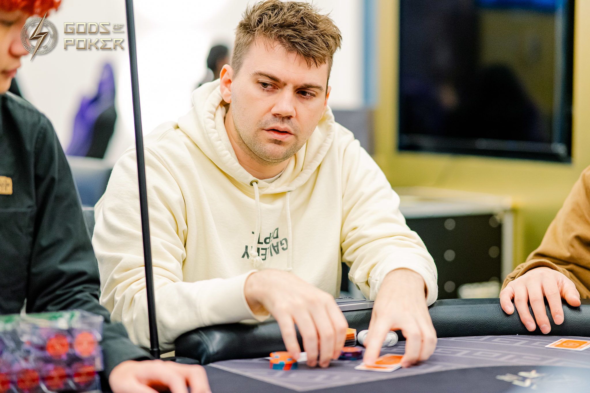 Man in light hoodie playing poker, focused on his cards and chips.