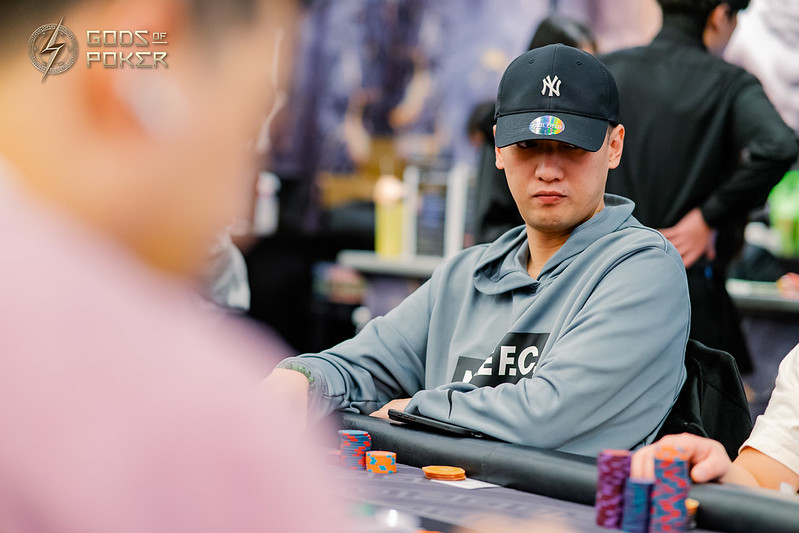 Man in Yankees cap and grey hoodie plays poker at a casino table.