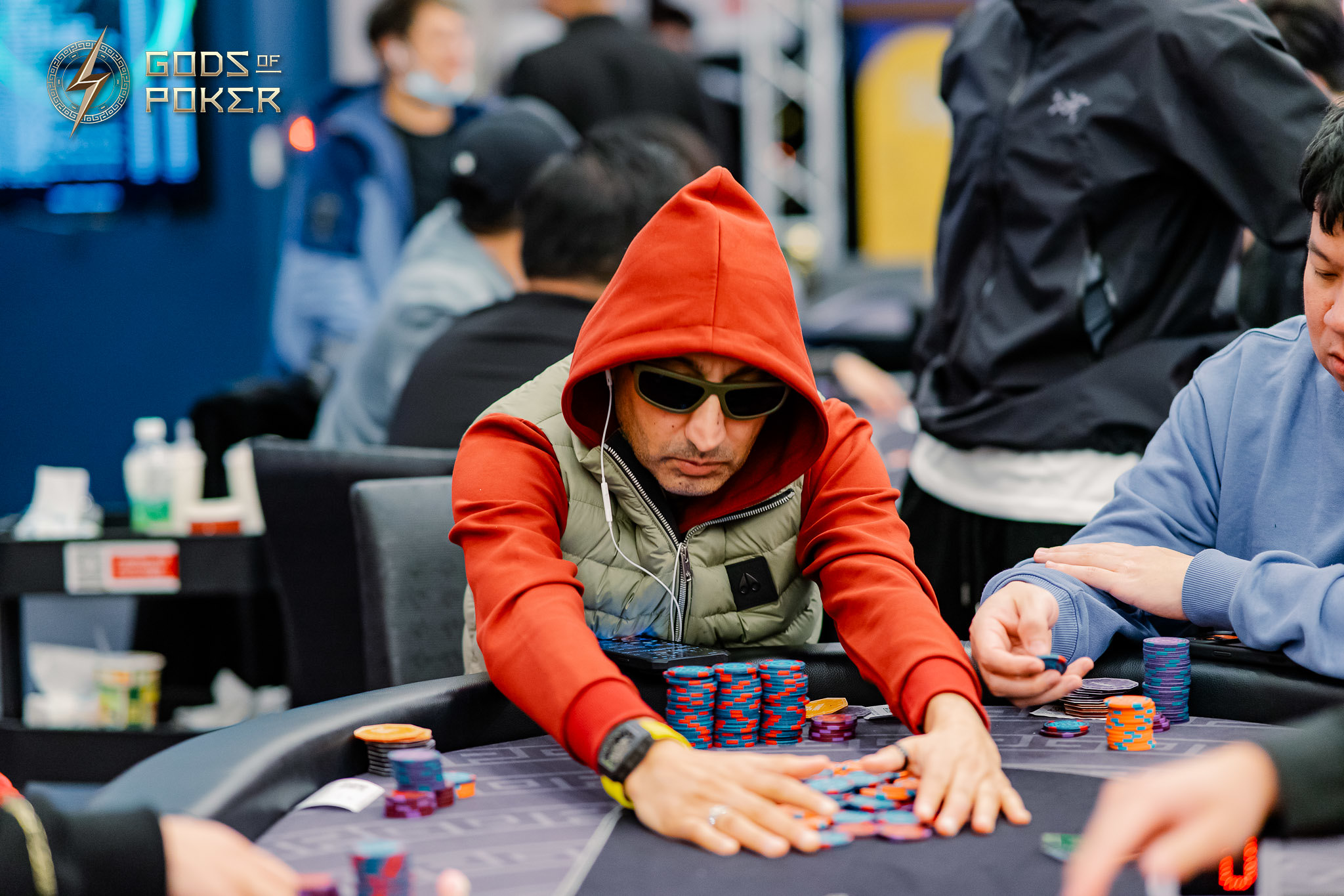 Man in red hoodie and sunglasses playing poker, moving chips on a table.
