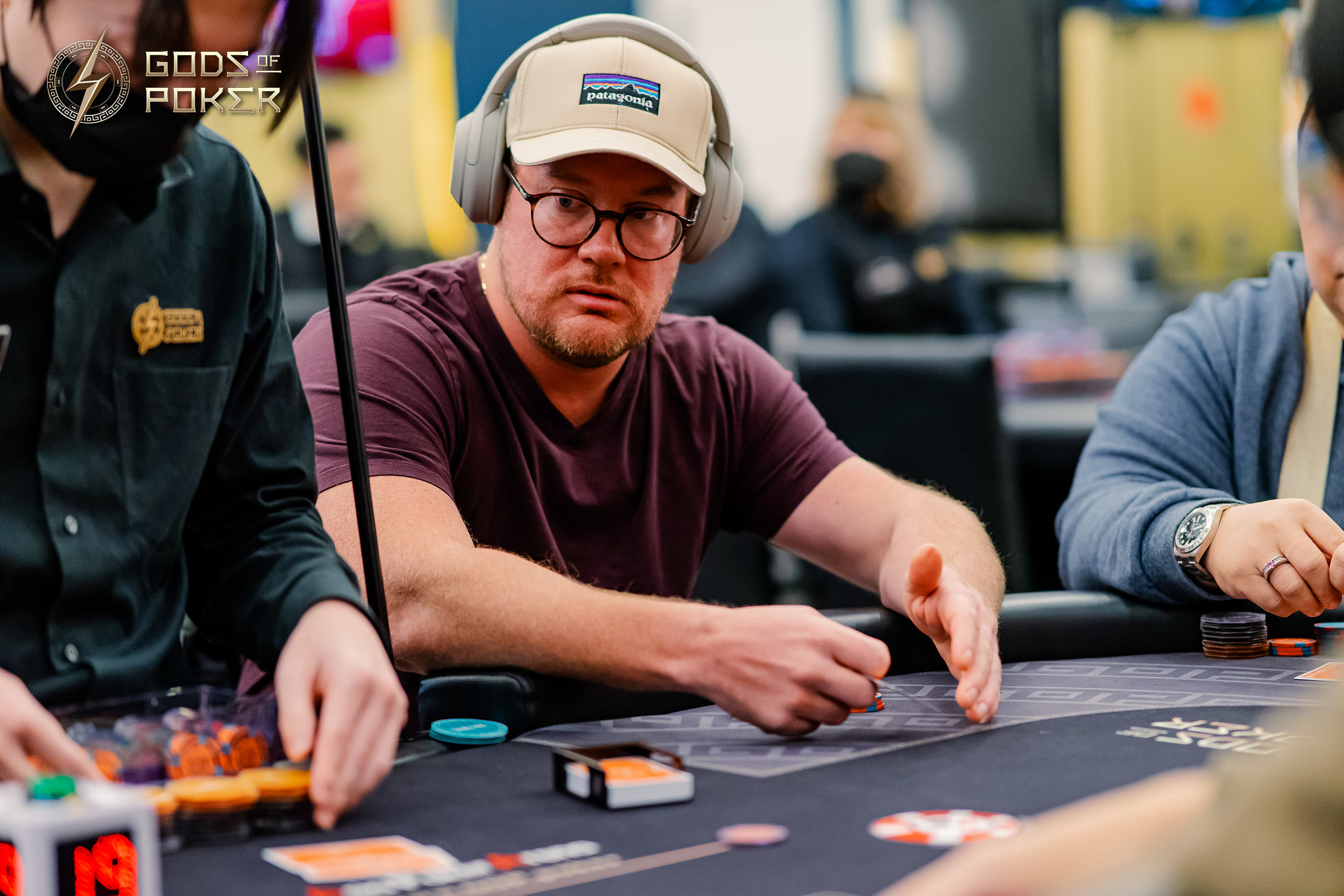 A man wearing glasses and a hat concentrates intently while playing poker at a table.