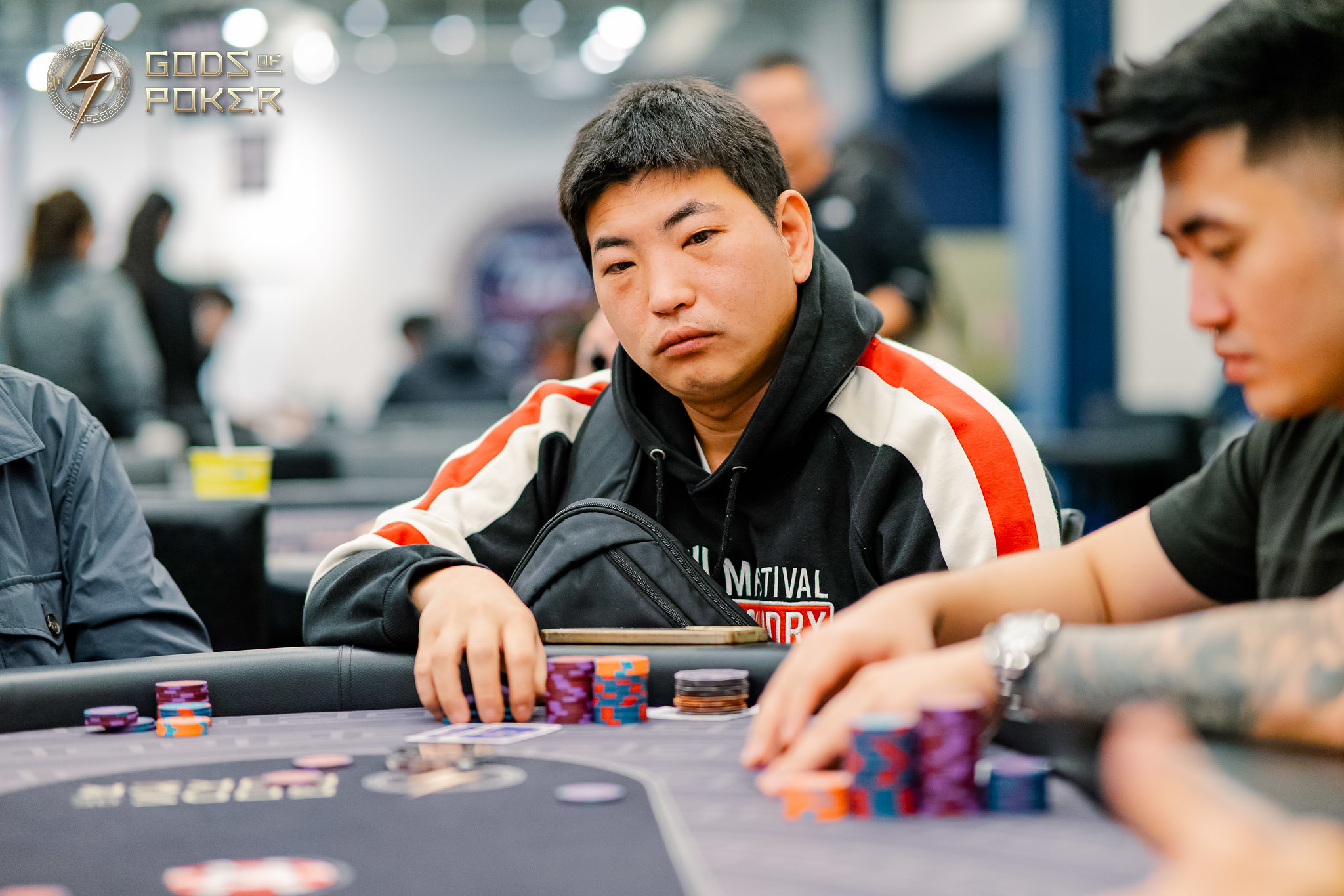 Man with black hair and serious expression sits at a poker table with chips.