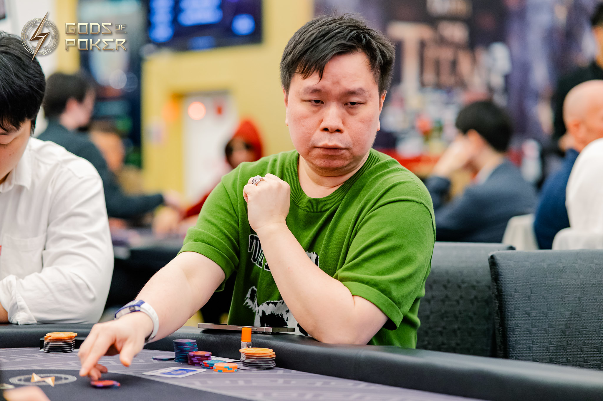 A focused Asian man in a green shirt plays poker, contemplating his next move.