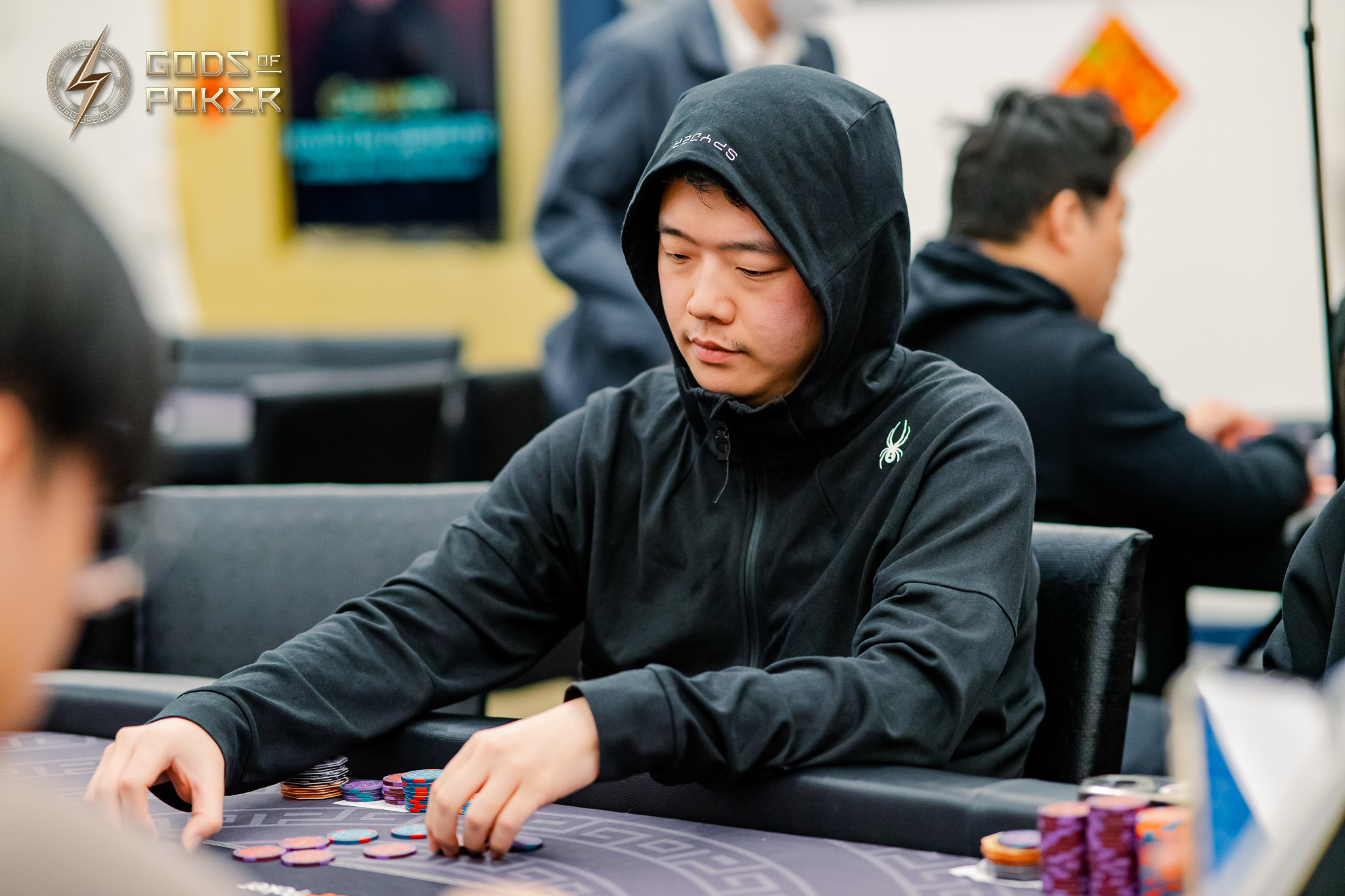Young man in black hoodie intently playing poker at a table with chips.