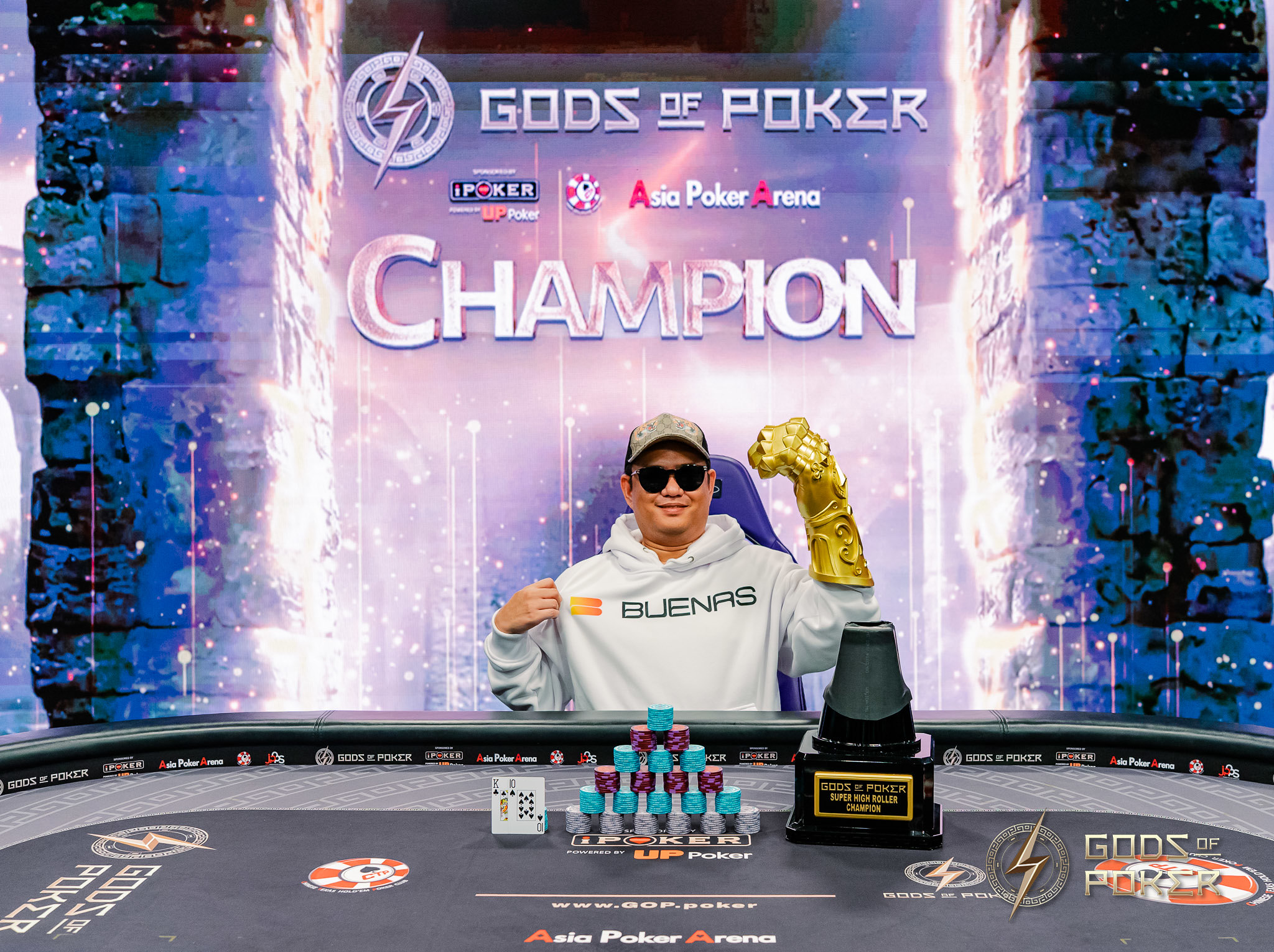Poker champion in hoodie and sunglasses holding golden gauntlet at table with trophy.