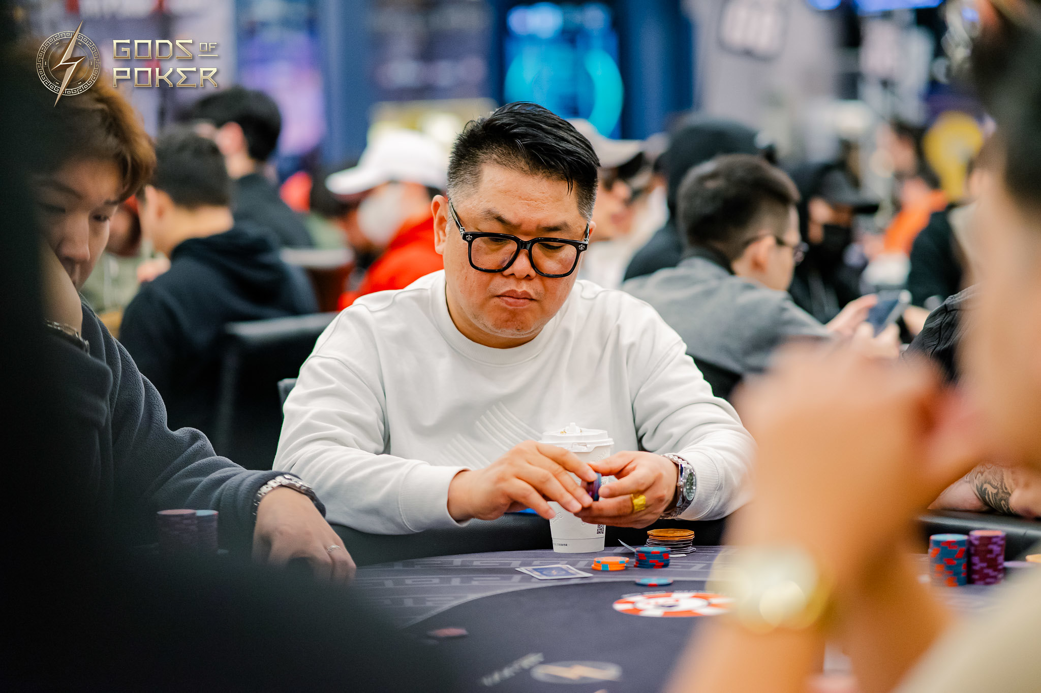 A man in glasses intently plays poker, holding chips at a casino table.