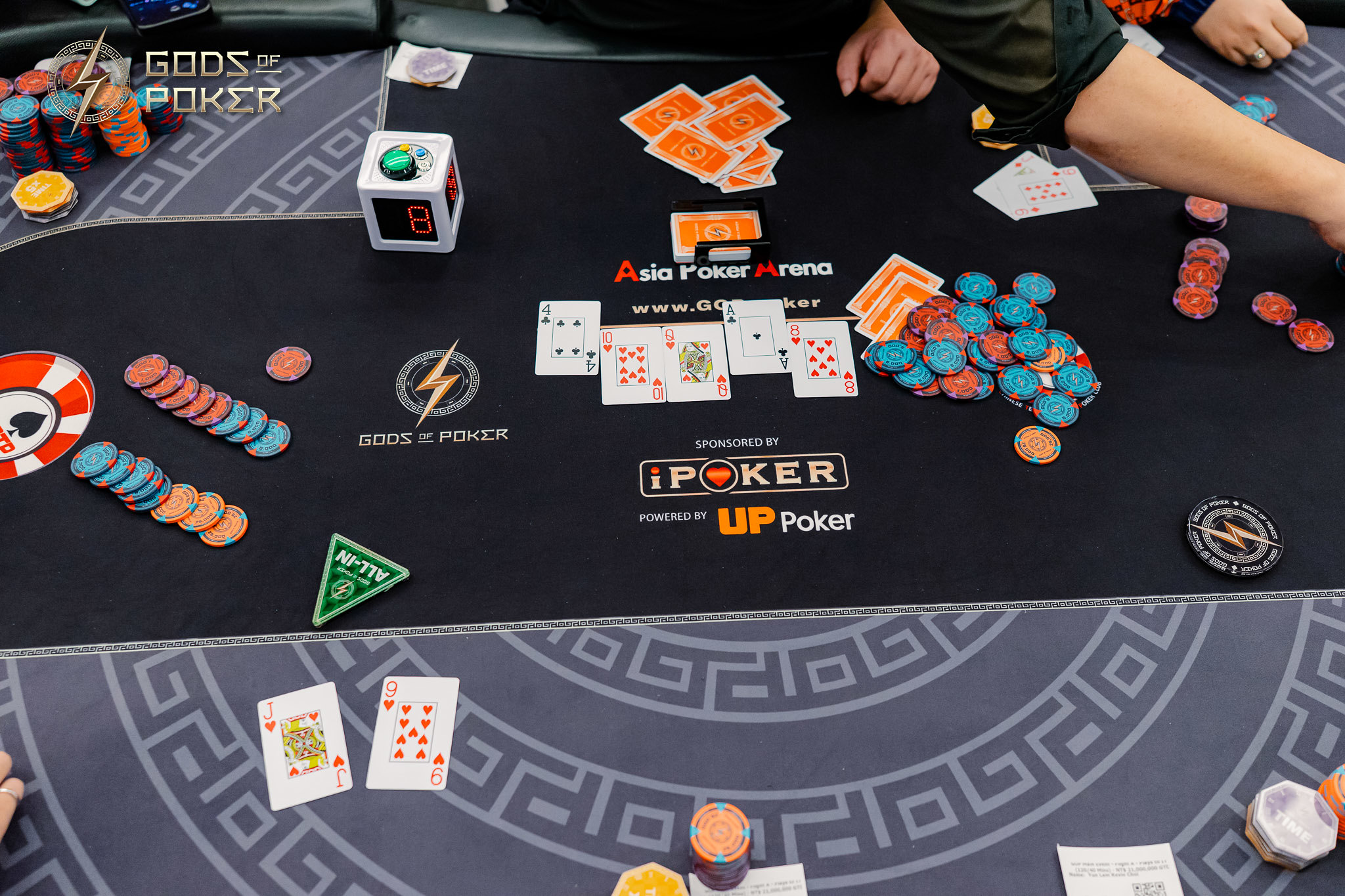 Overhead view of a poker table with cards, chips, and players' hands during a game.