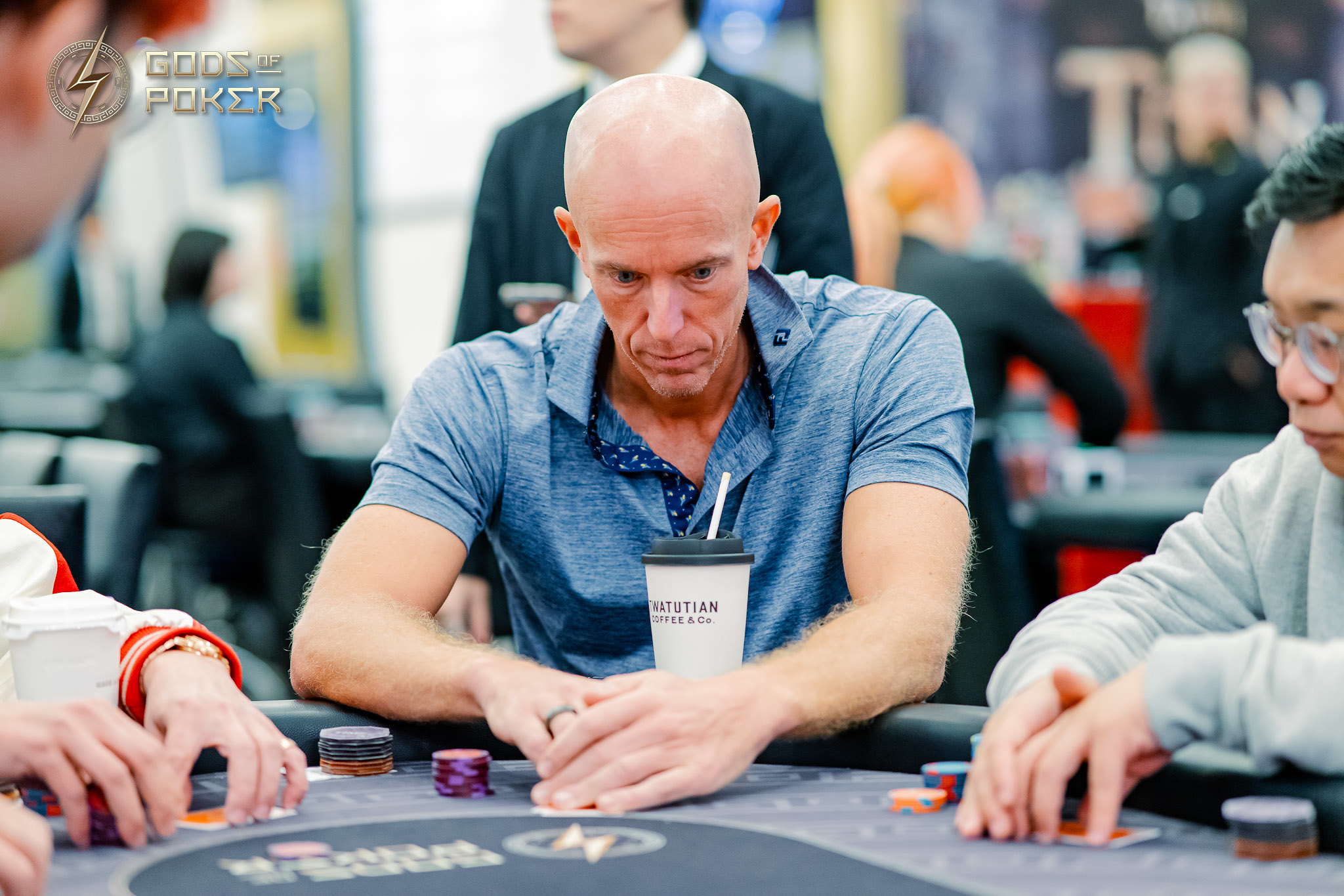 Bald man intensely focuses on his cards during a poker game, surrounded by chips.