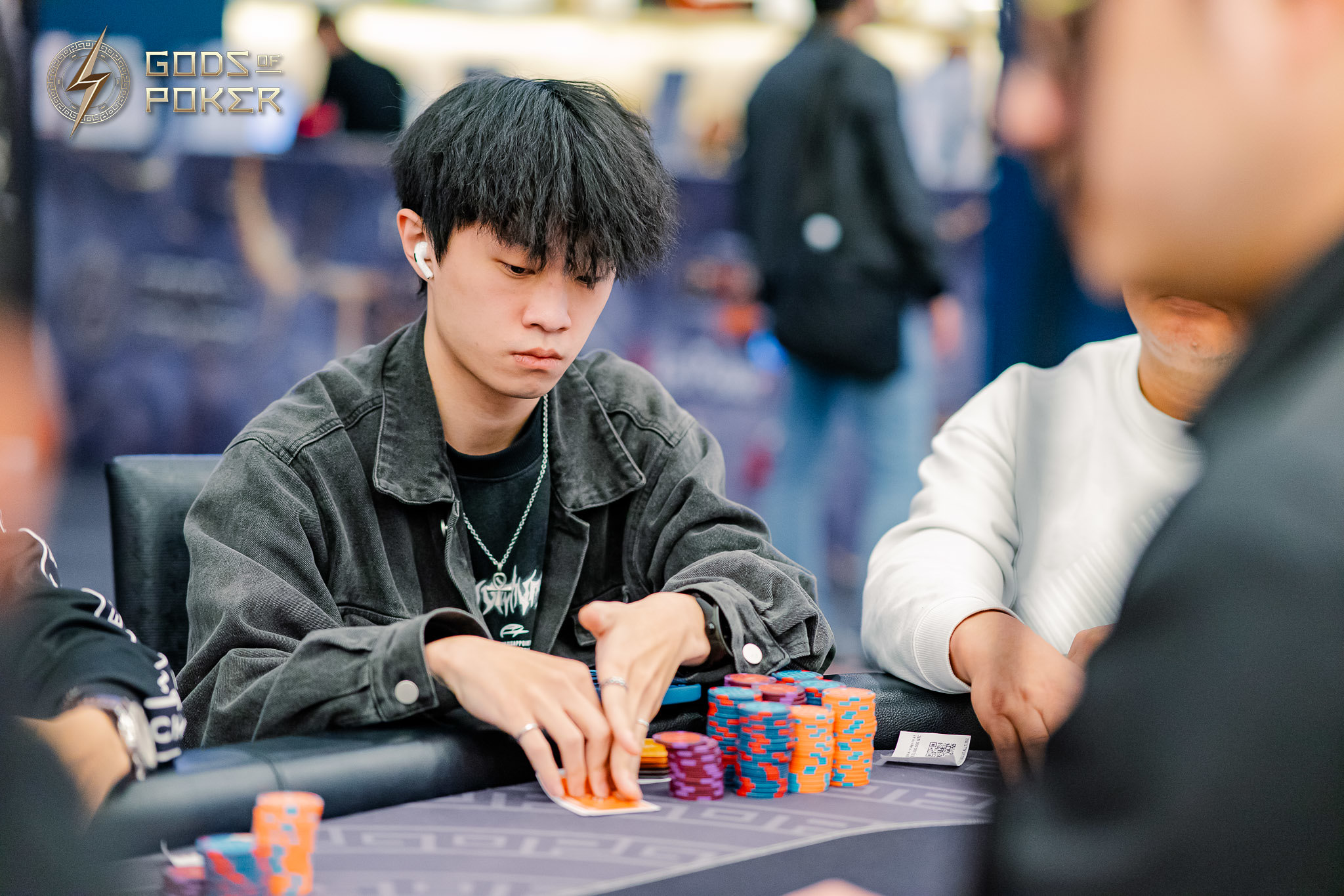 Young Asian man intently playing poker, hands on chips and cards.