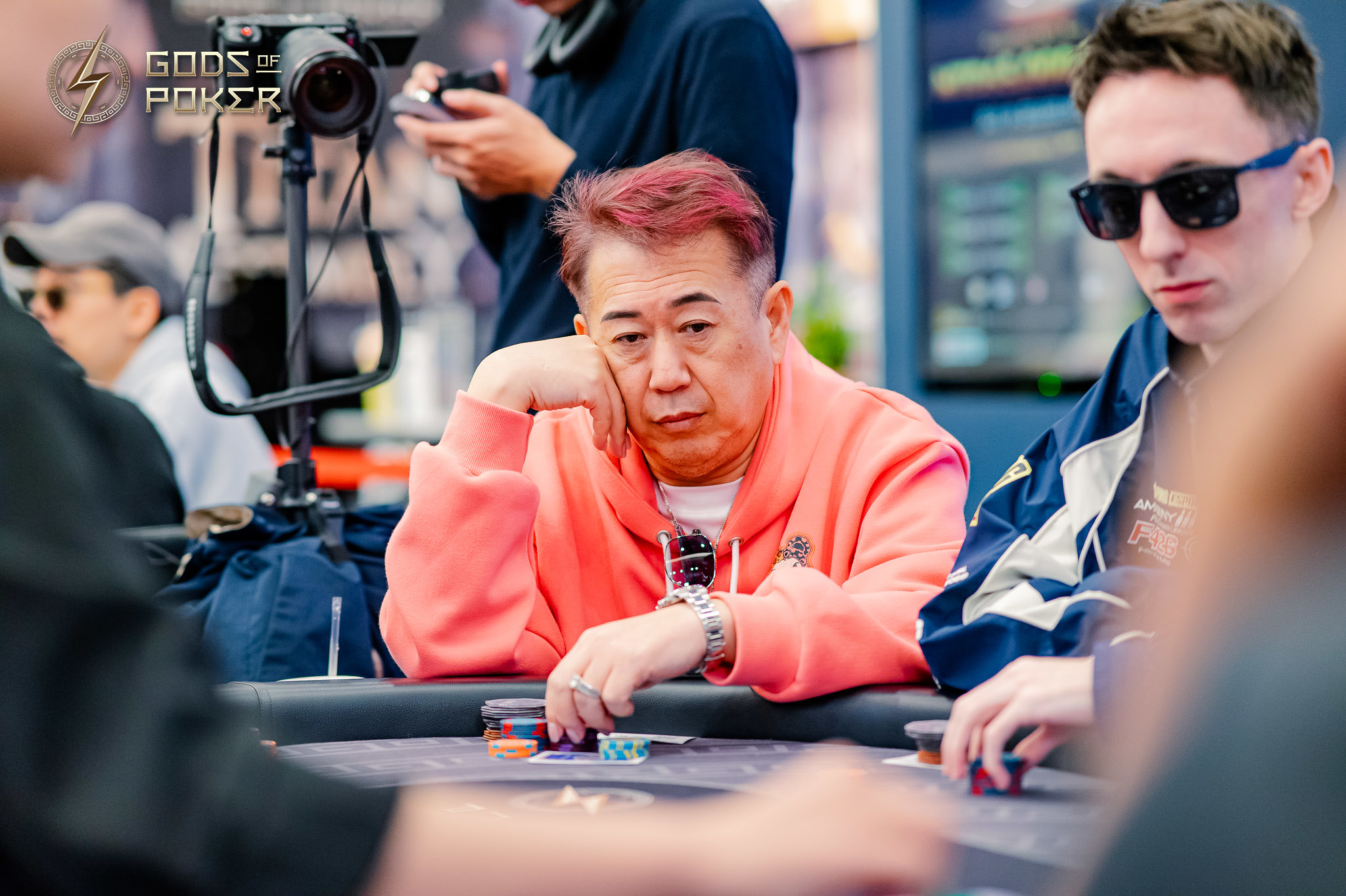 A pensive man with red hair in a coral hoodie sits at a poker table.