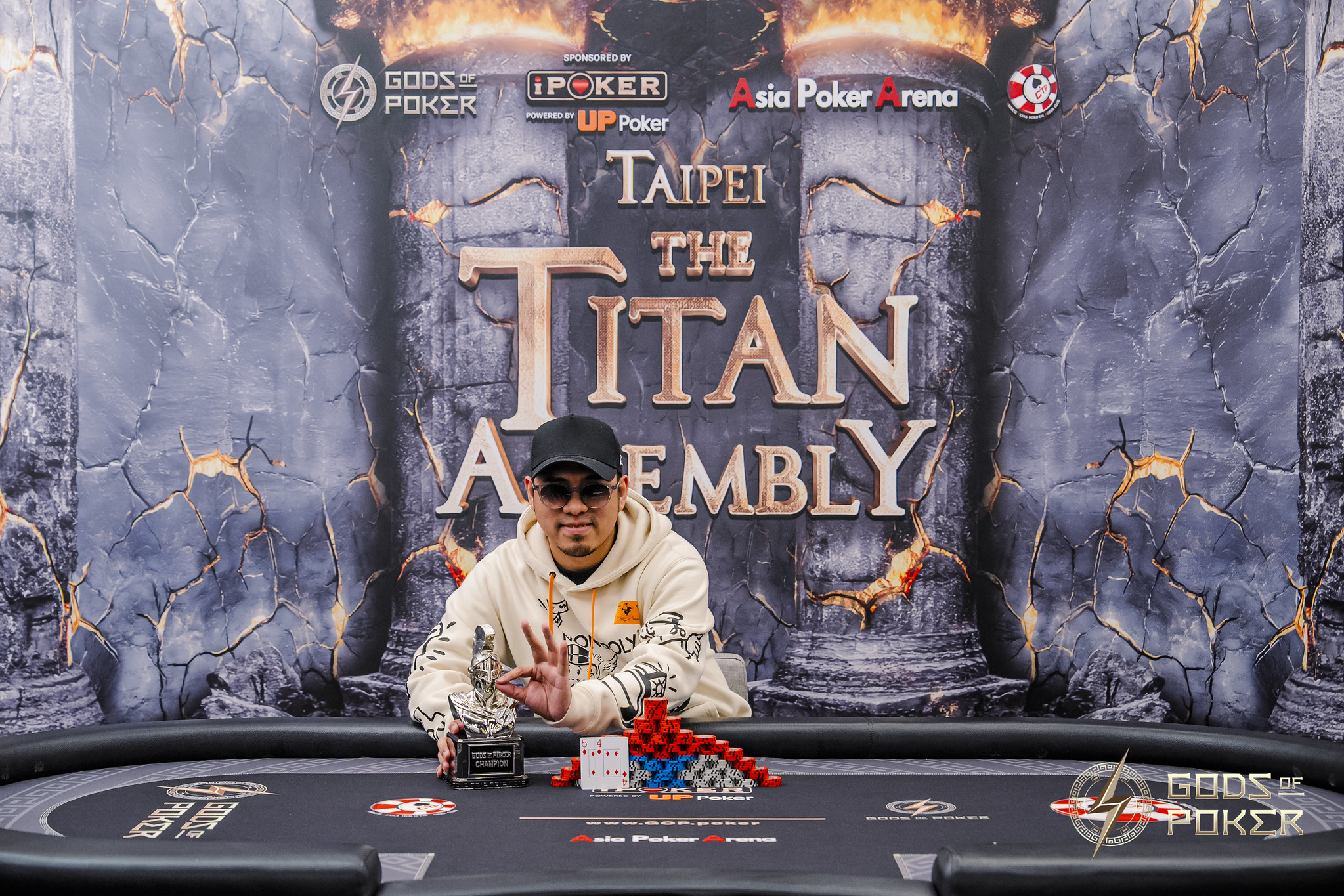 Man celebrating at a poker table with chips, in front of a 'Taipei The Titan Assembly' banner.