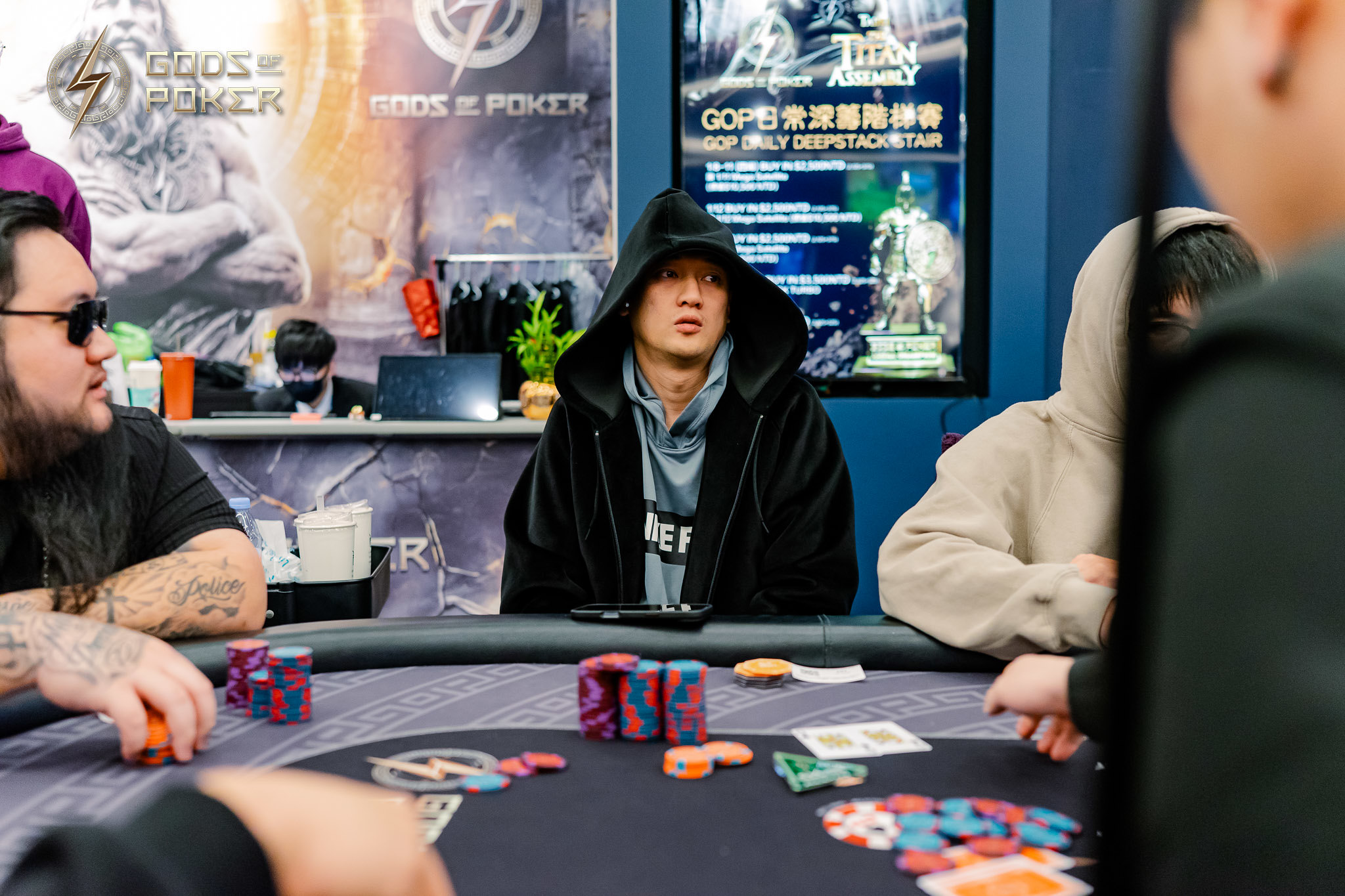 Man in black hooded robe at a poker table with chips and cards.