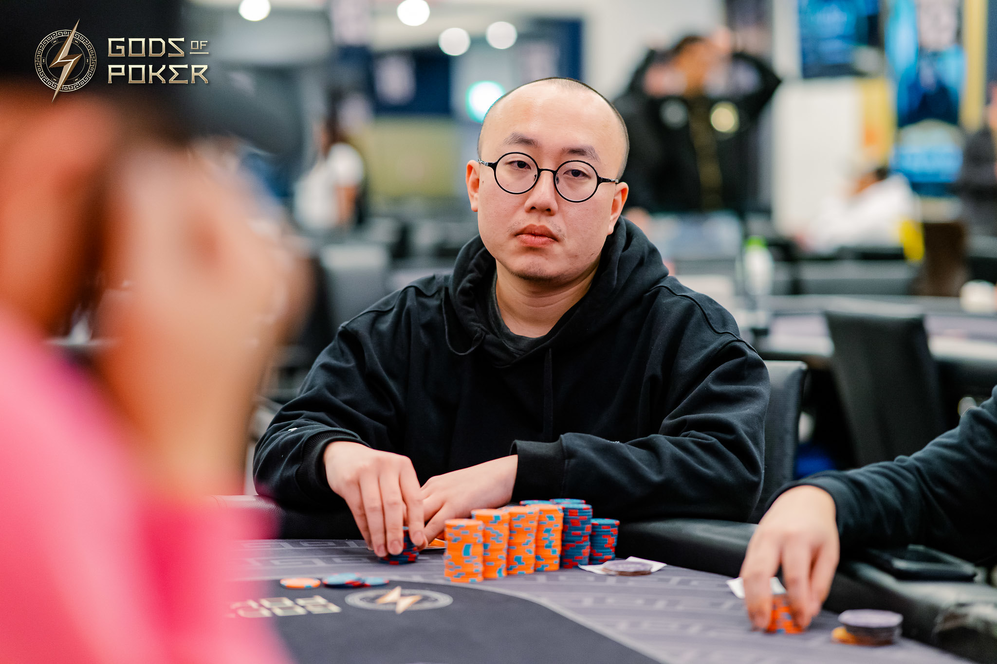 Bald man in glasses at poker table with stack of chips, looking intently.