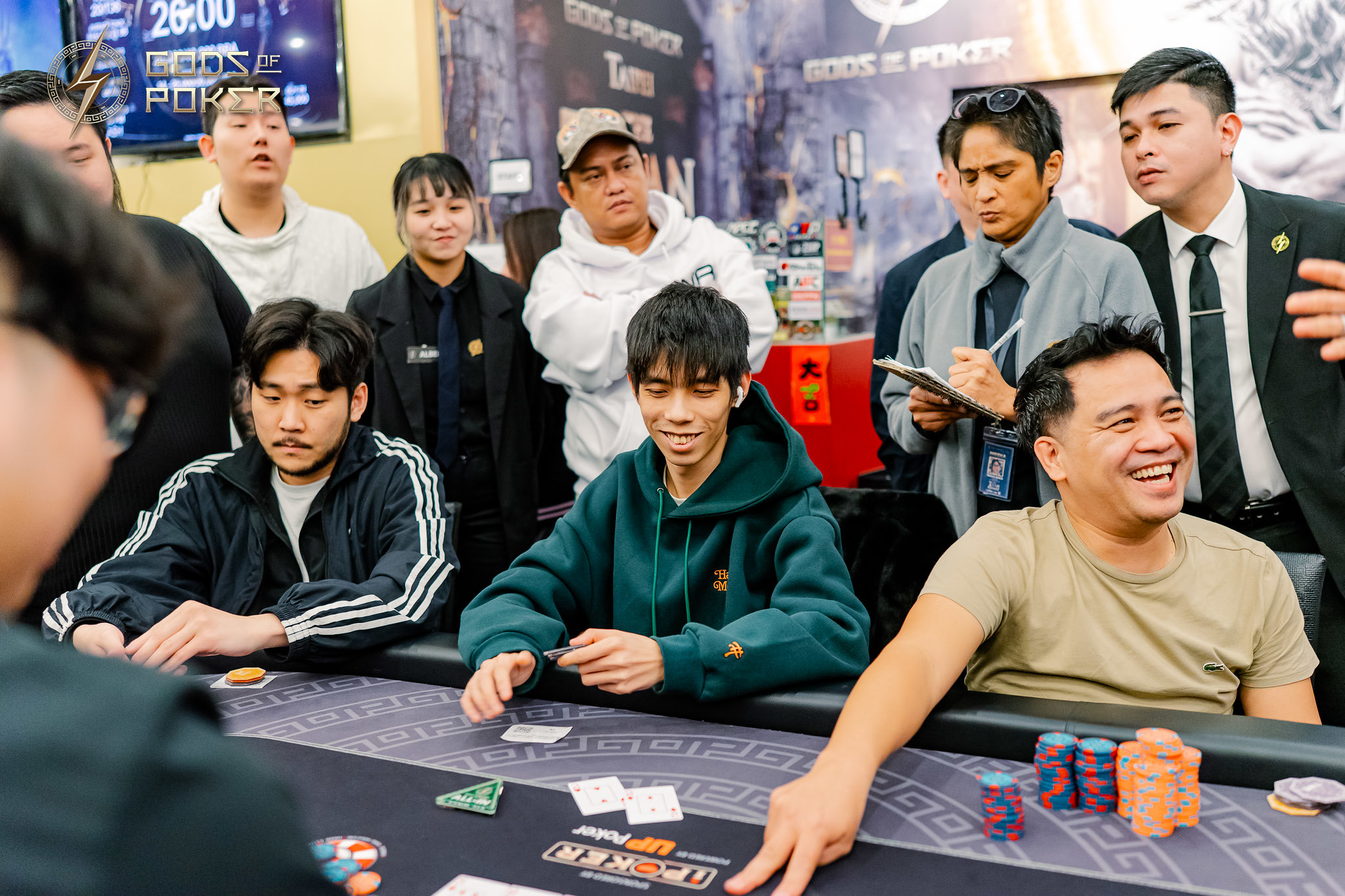 Group of people playing and observing poker at a busy tournament table.