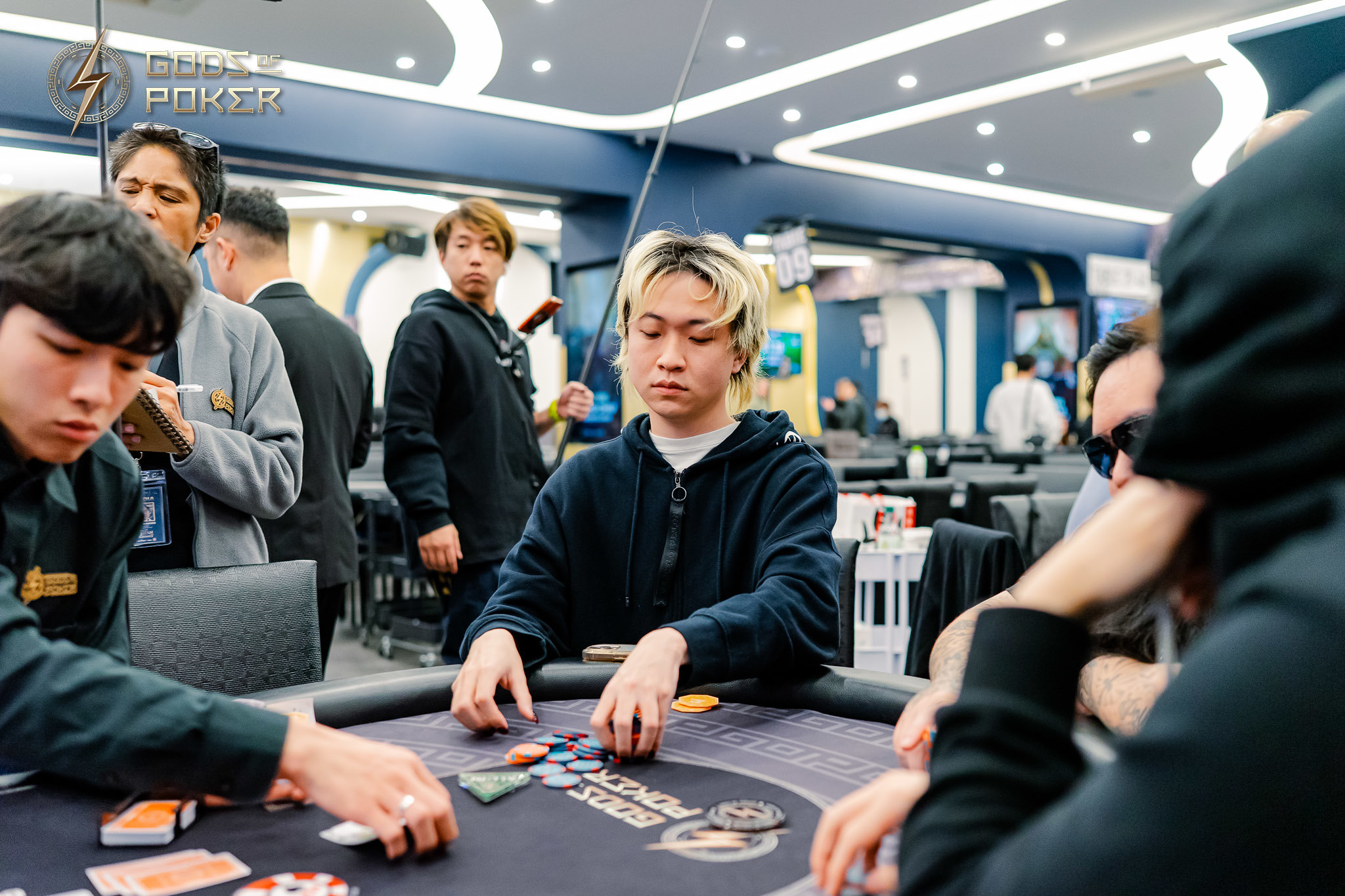 Young man intently playing poker, surrounded by other players and casino atmosphere.