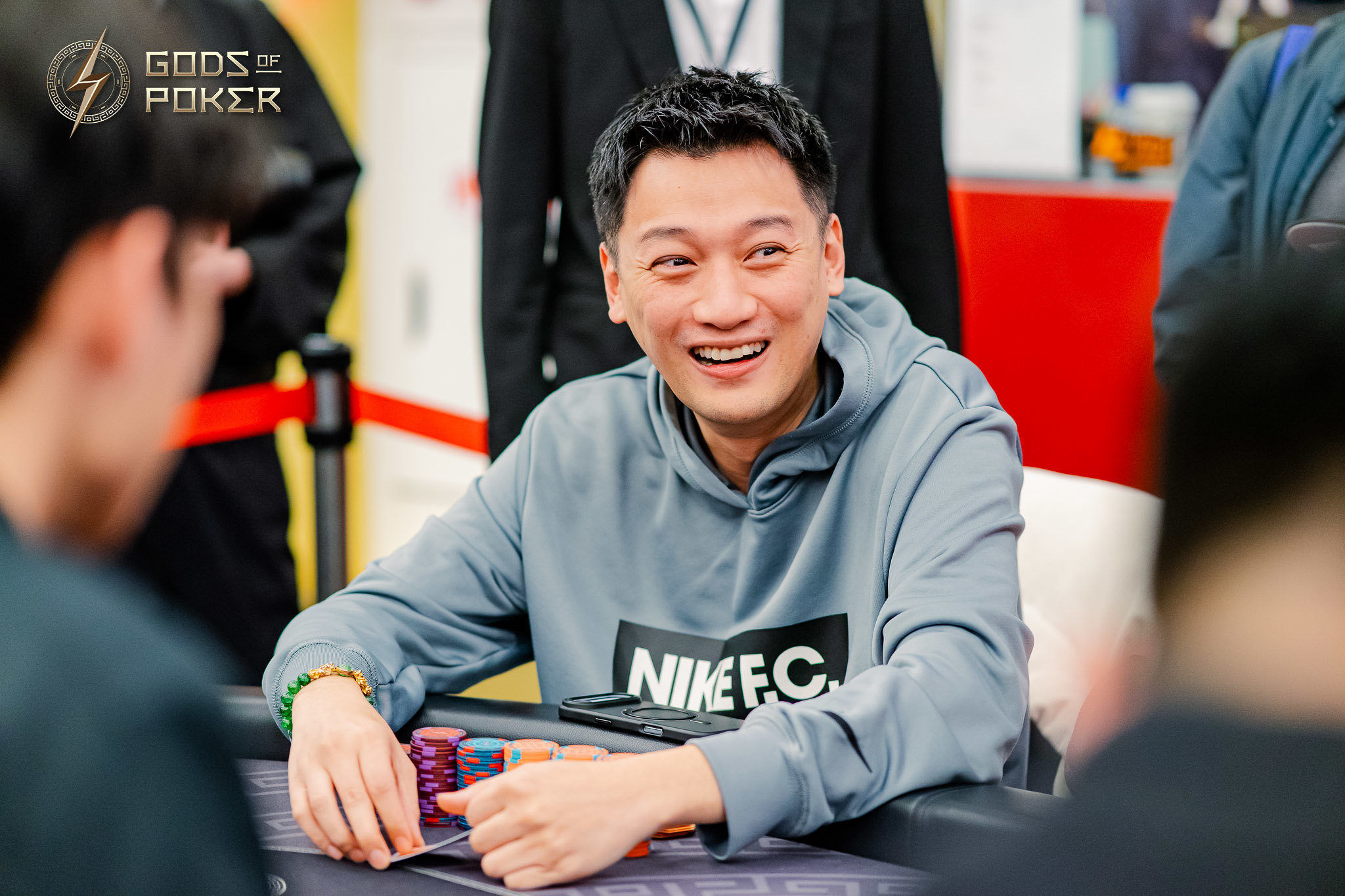 Smiling man in a Nike FC hoodie playing poker, with chips on the table.