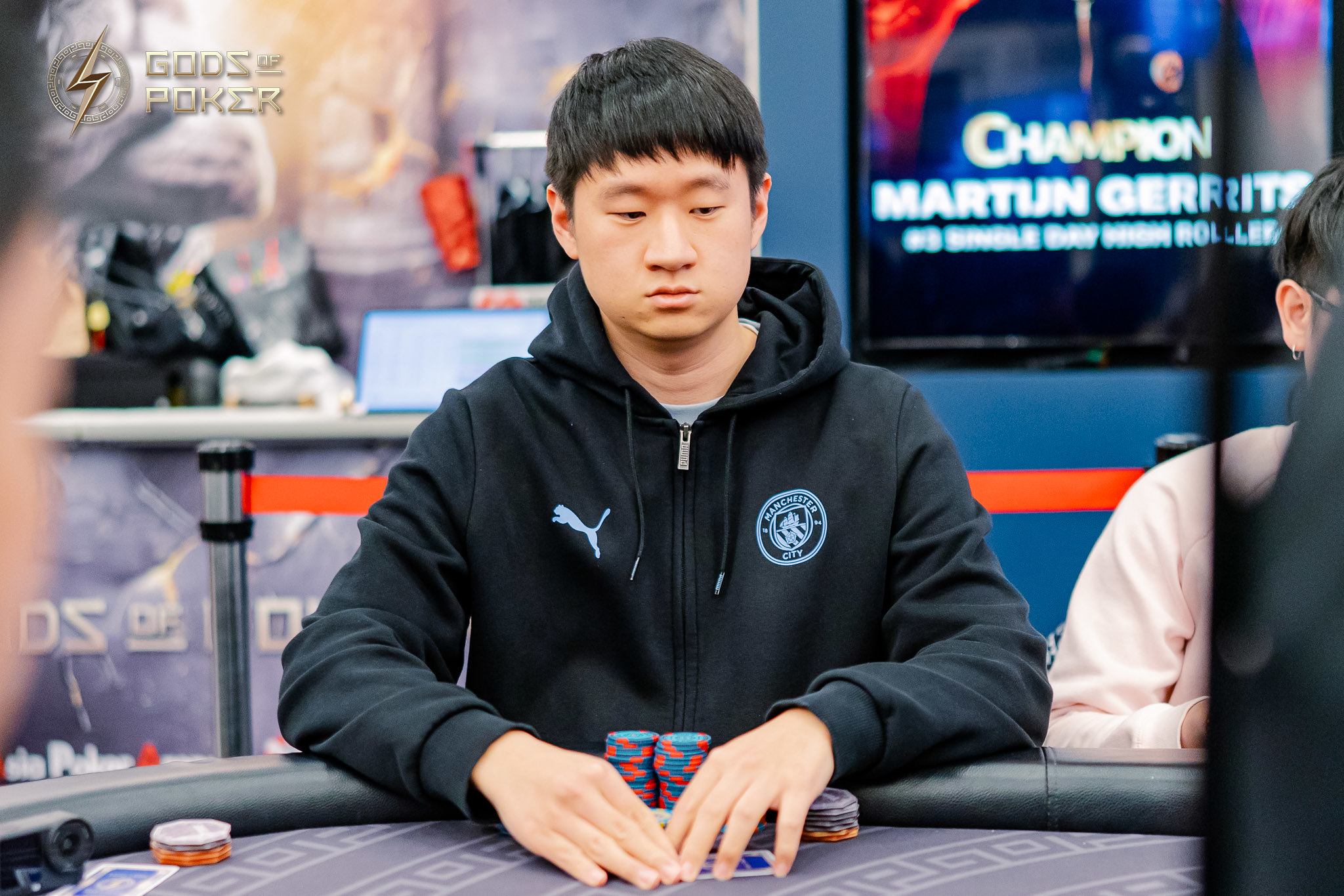 Young Asian man intently focused at a poker table with chips in front of him.