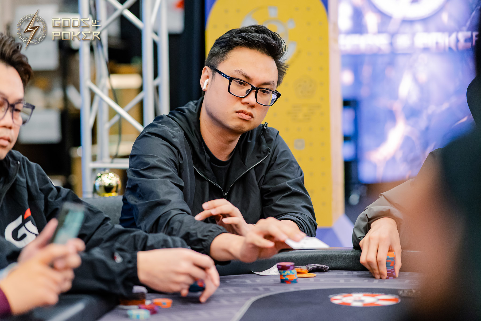Man in glasses intently playing poker at a casino table with chips and cards.