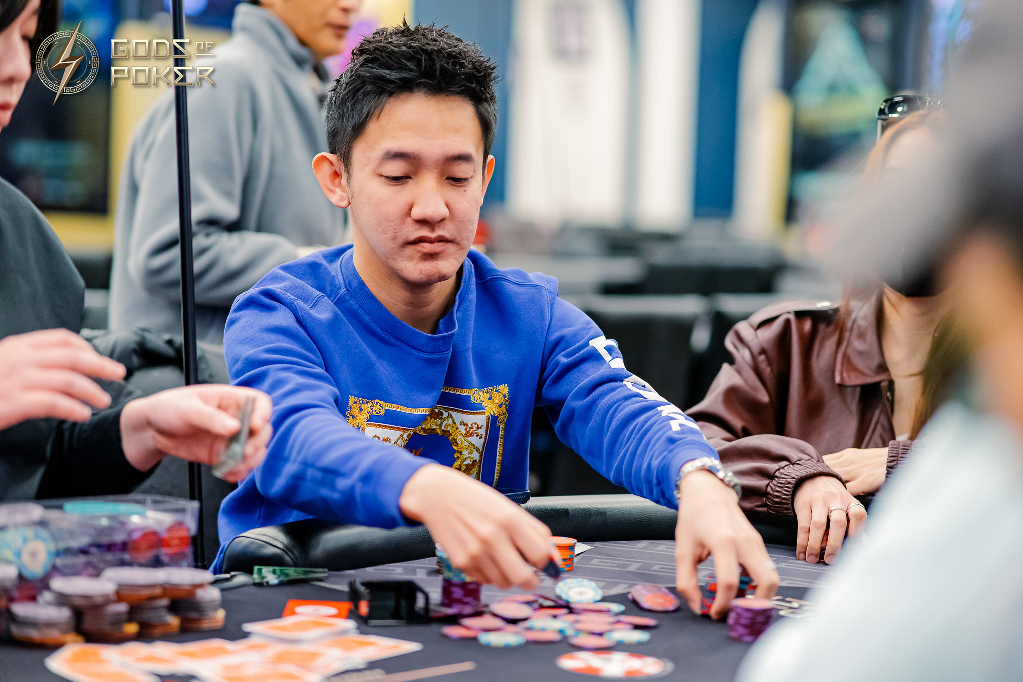 Young Asian man in blue shirt intently playing poker at a table with chips.