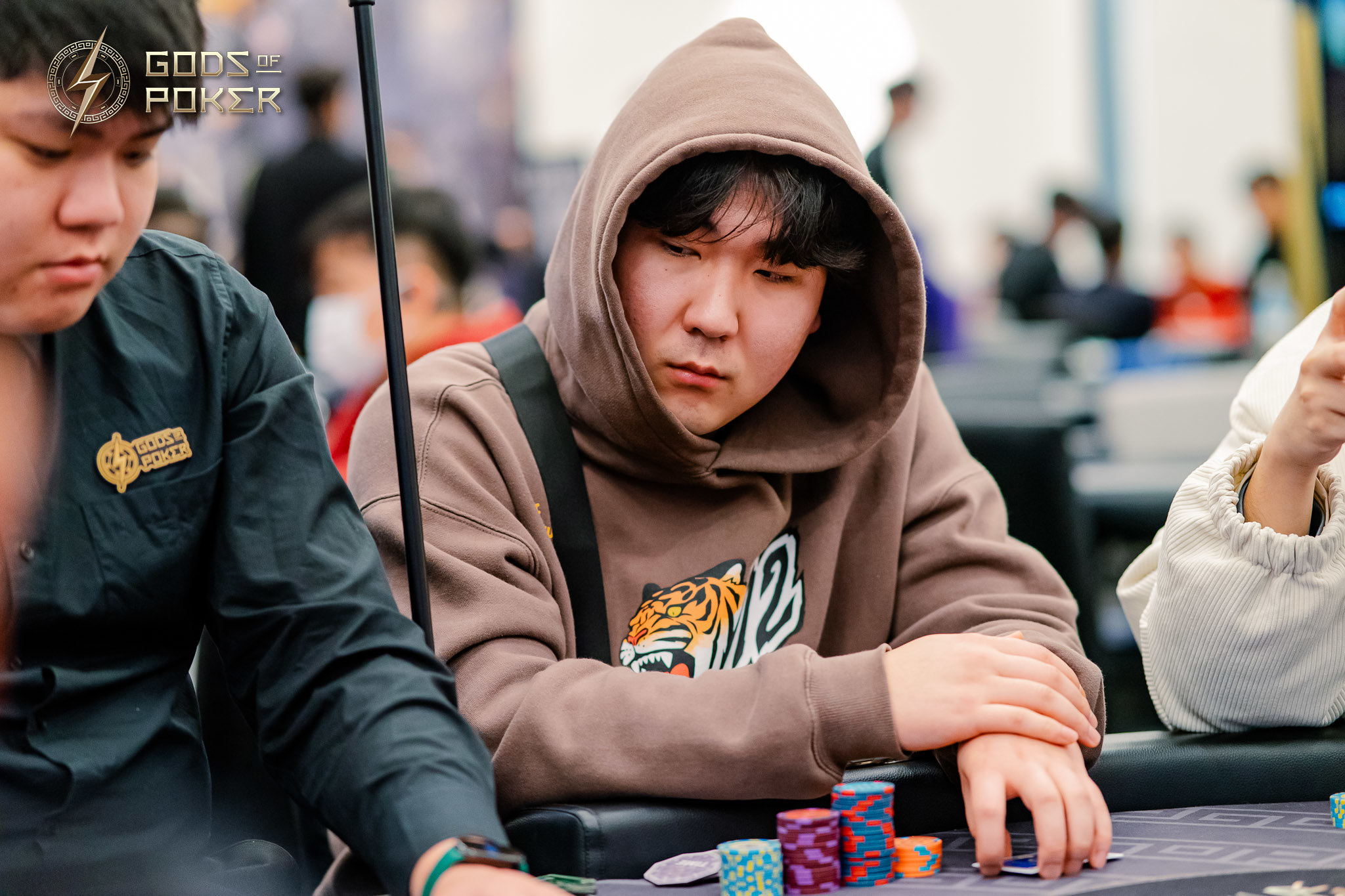 Man in a brown hoodie intently watches poker chips at a card table.
