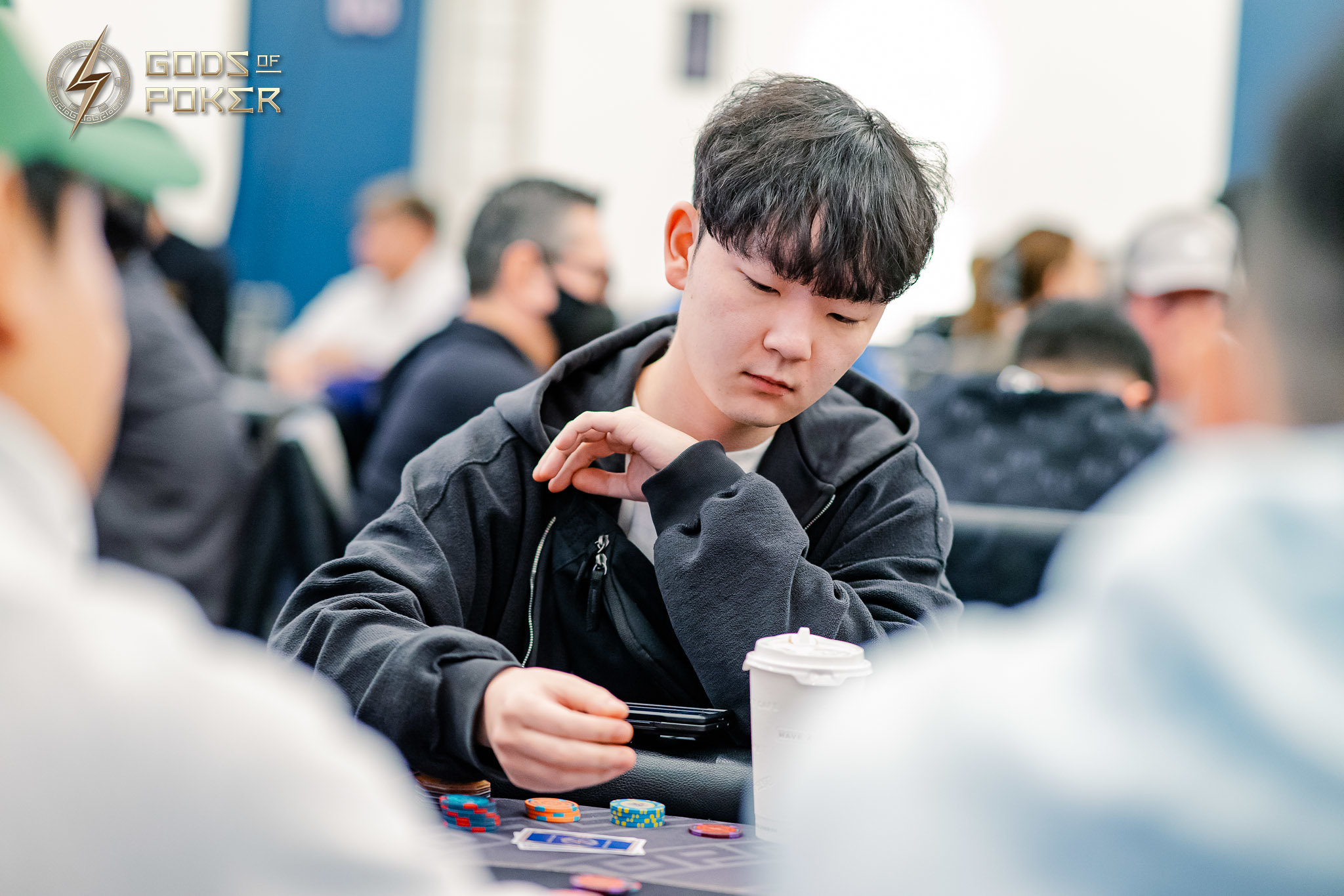 Young Asian man intently playing poker, looking down at his cards at a table.