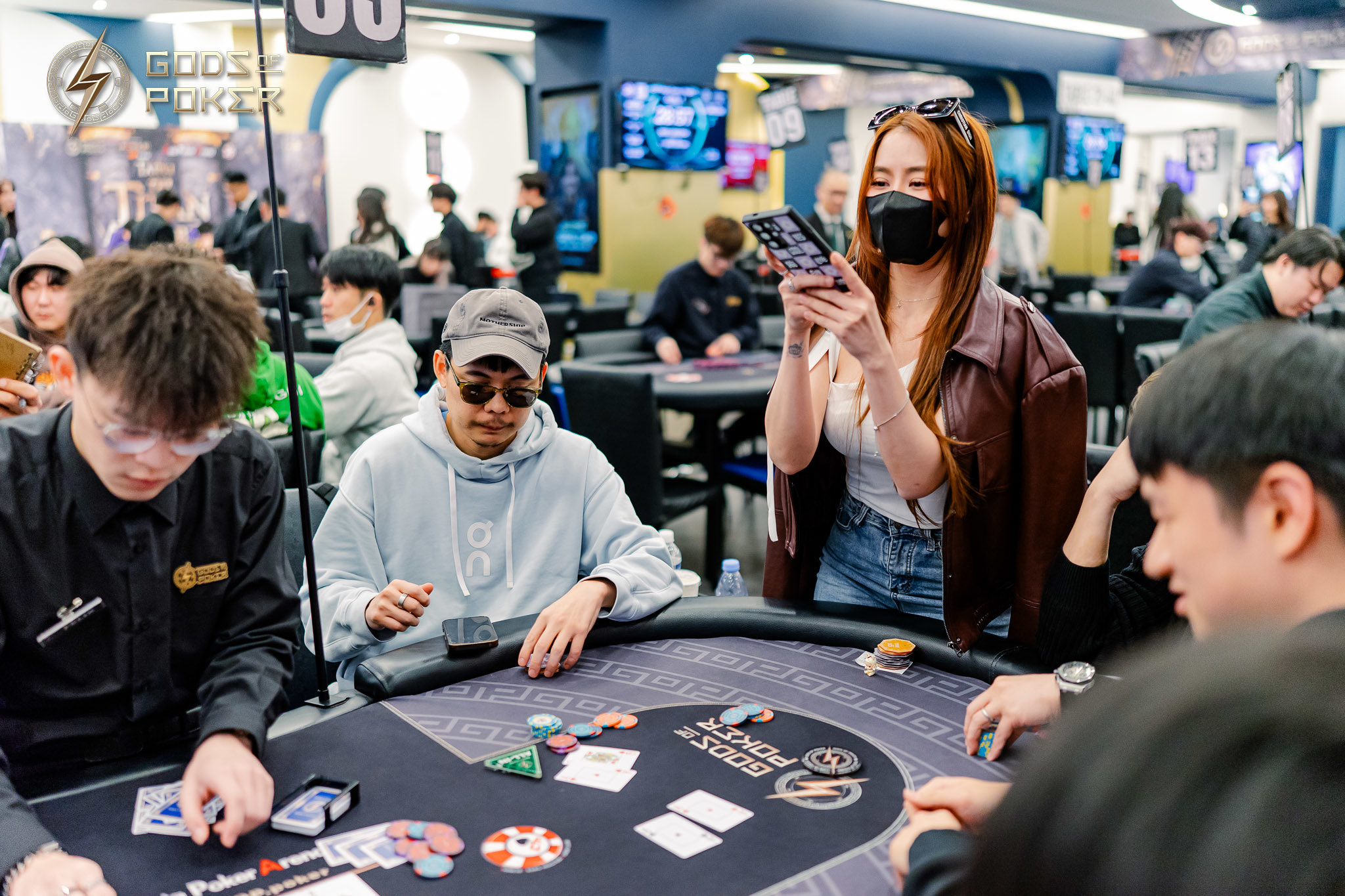 People playing poker at a casino table, one woman looks at her phone.