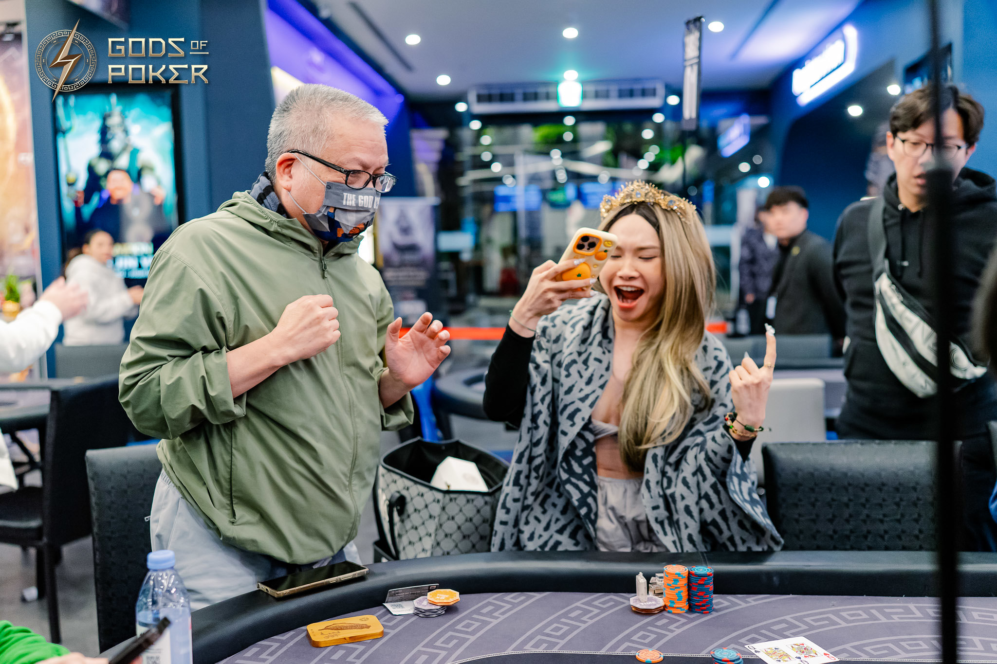 A woman enthusiastically takes a selfie at a poker table as a man observes her.