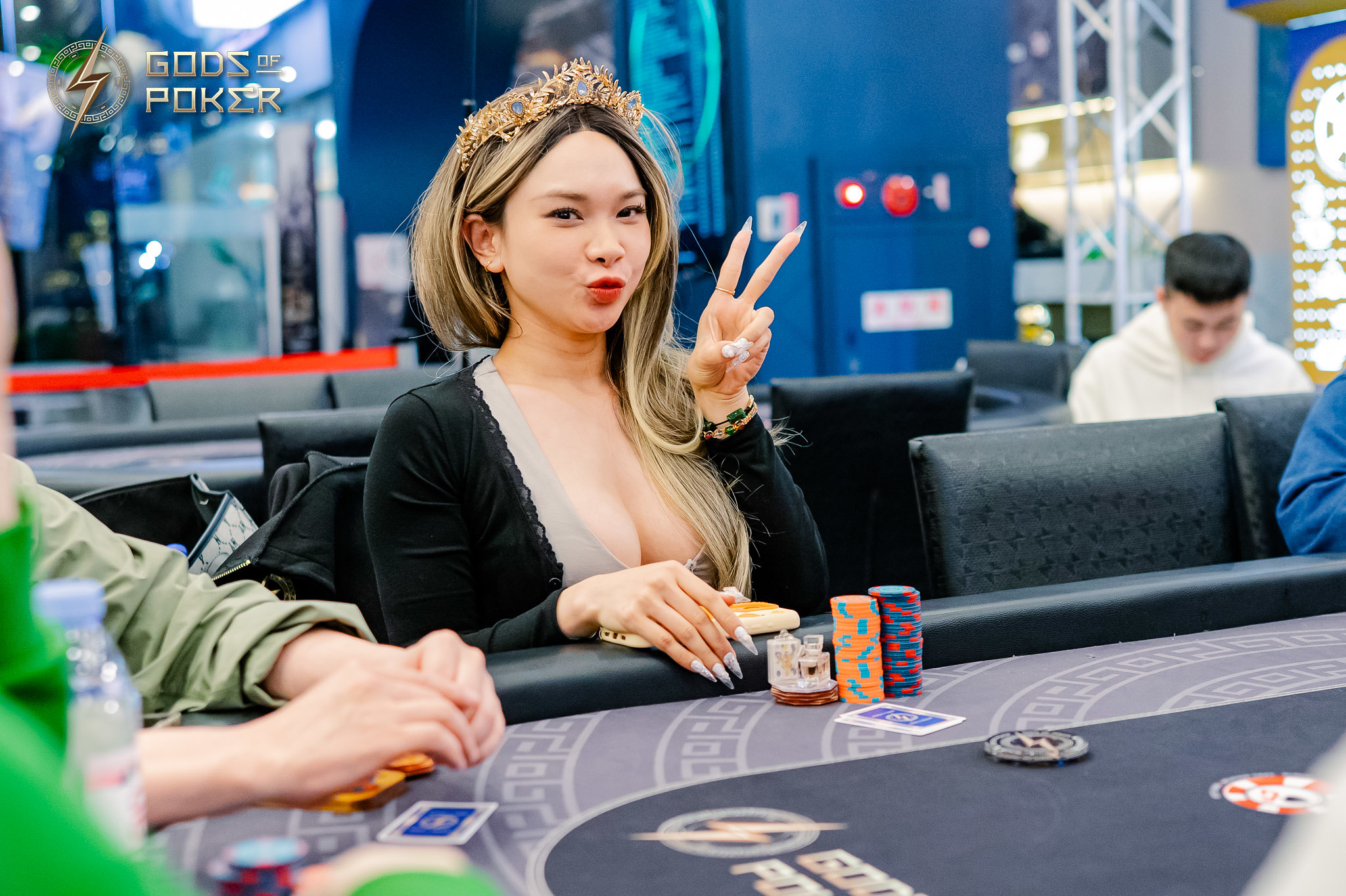 Woman wearing a crown-like headband makes a peace sign at a poker table.