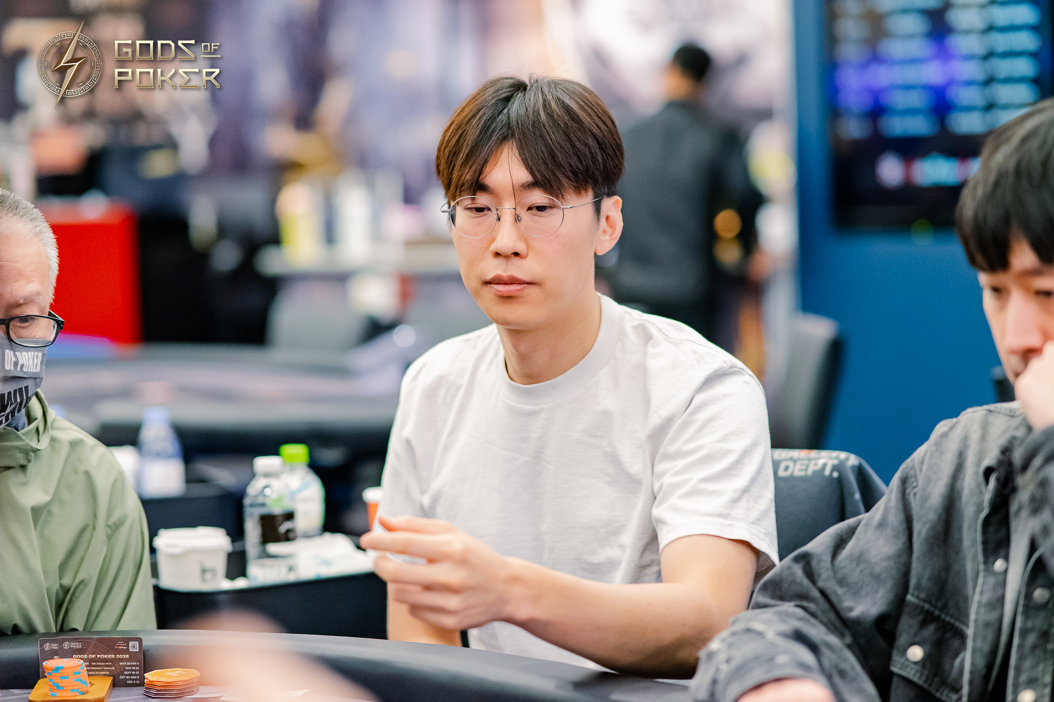 Young man in white t-shirt intensely focuses on cards at a poker table.