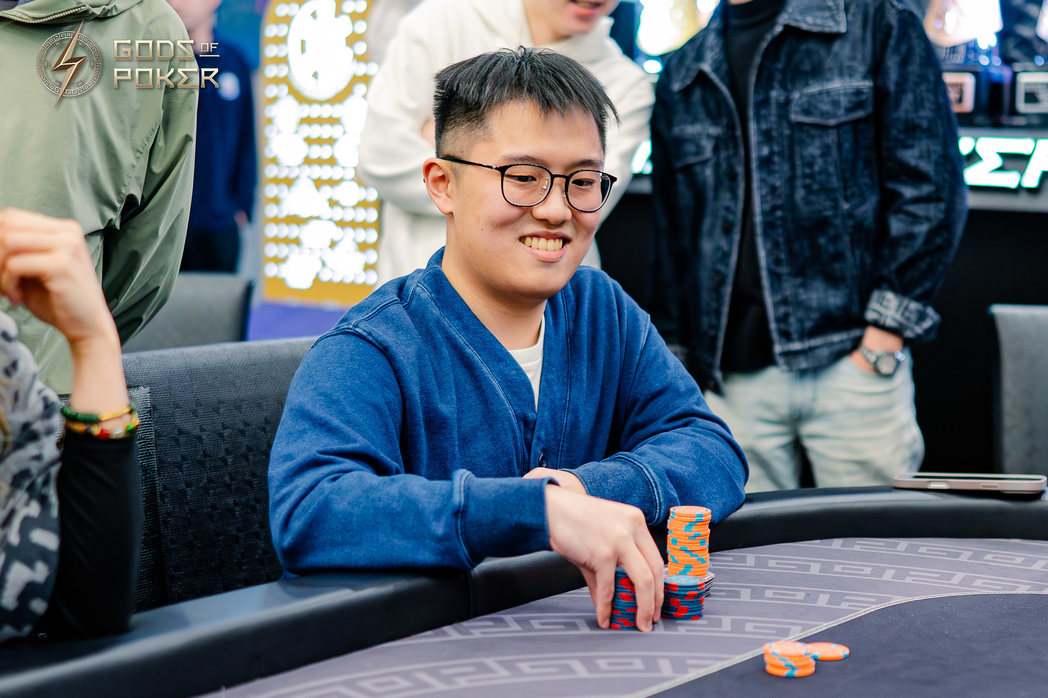Smiling man in glasses plays poker, reaching for a stack of chips on the table.