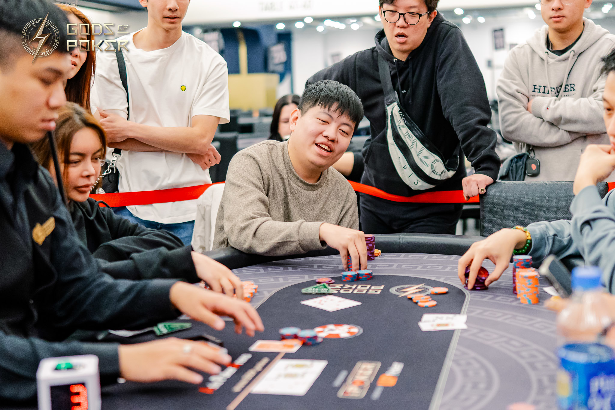 Smiling man in brown sweater playing poker with others at a card table.