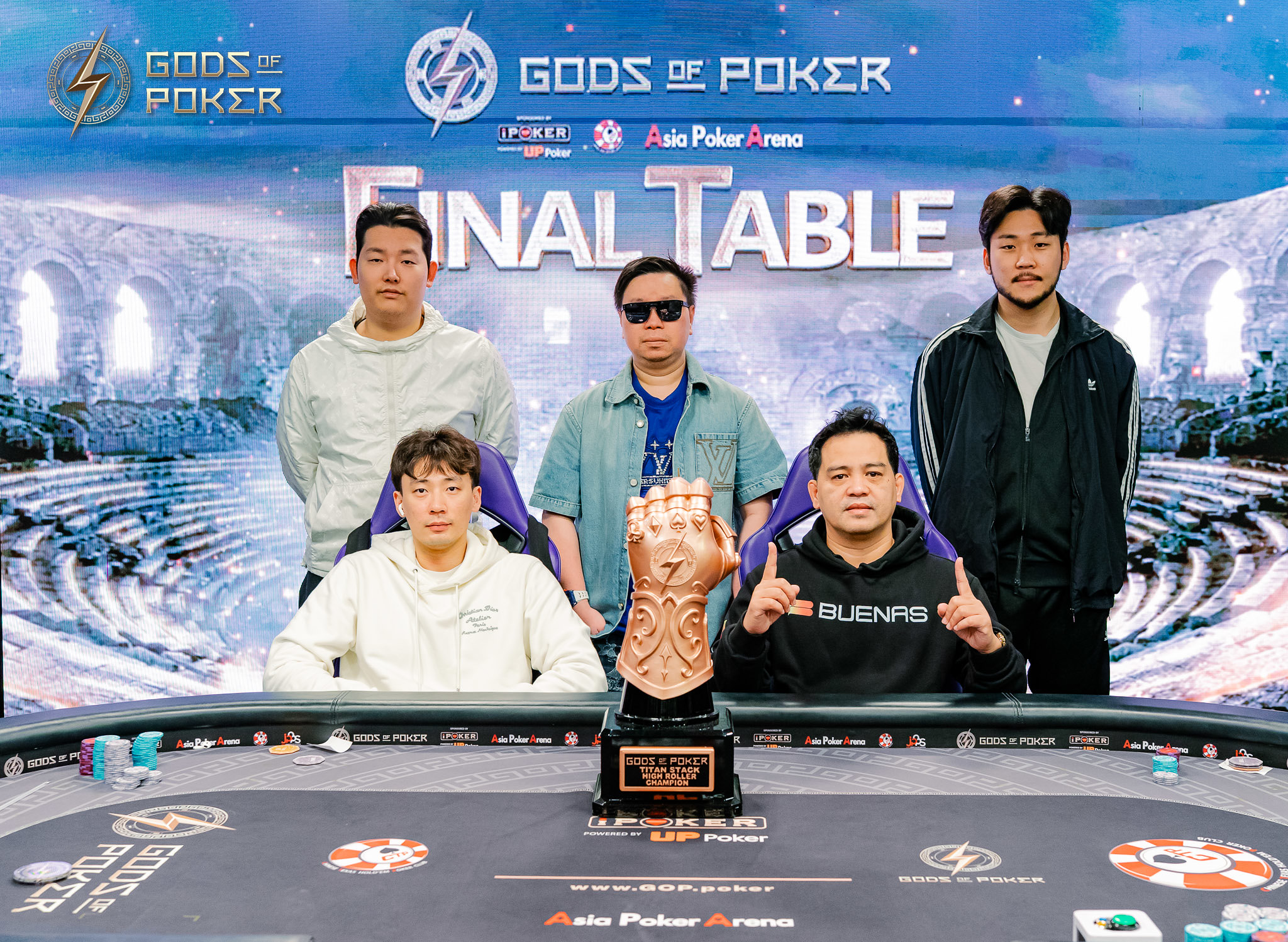 Five poker players stand with a golden trophy at the Gods of Poker final table.