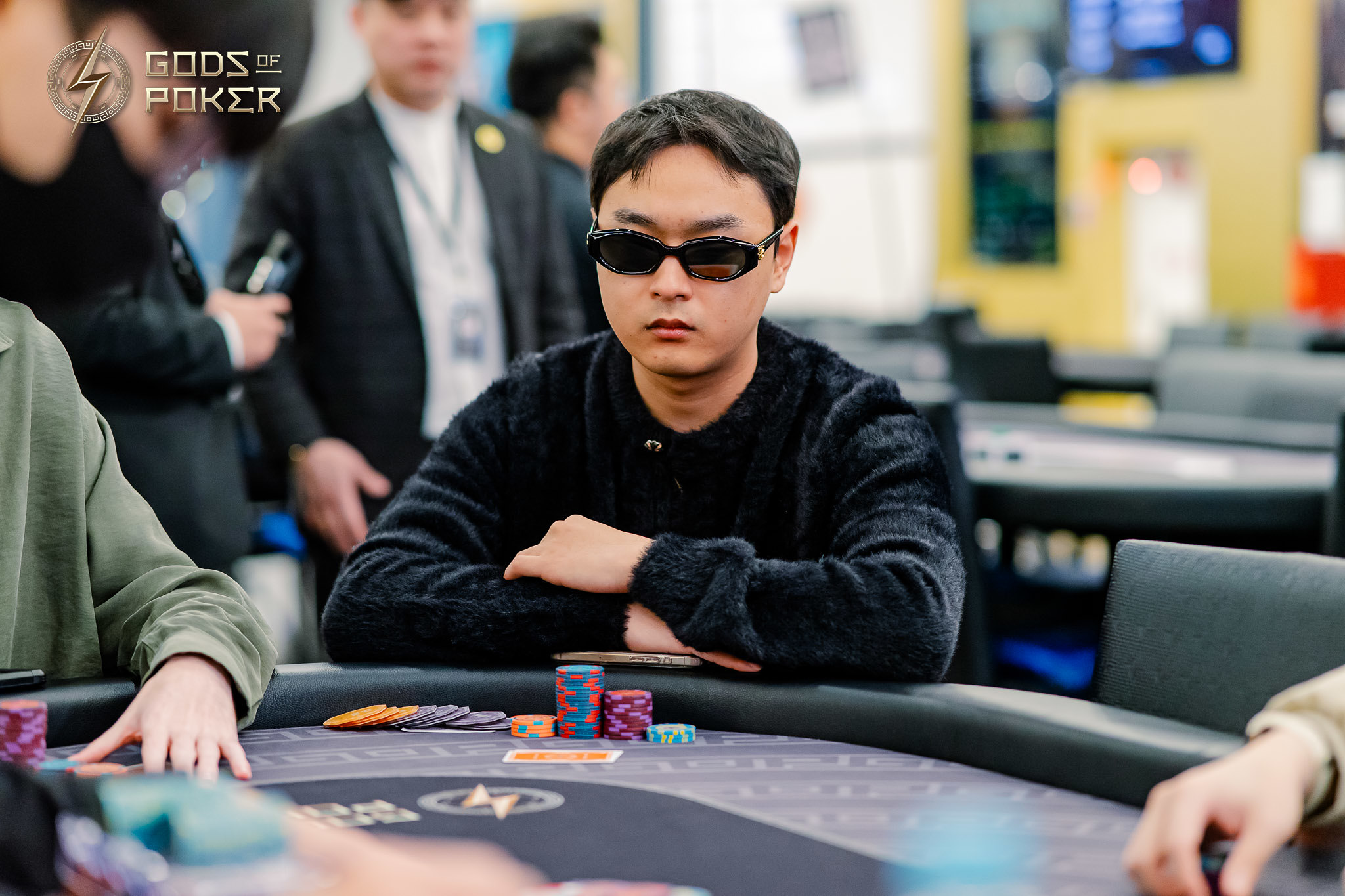 Man in black sunglasses and sweater intently focused at a poker table with chips.