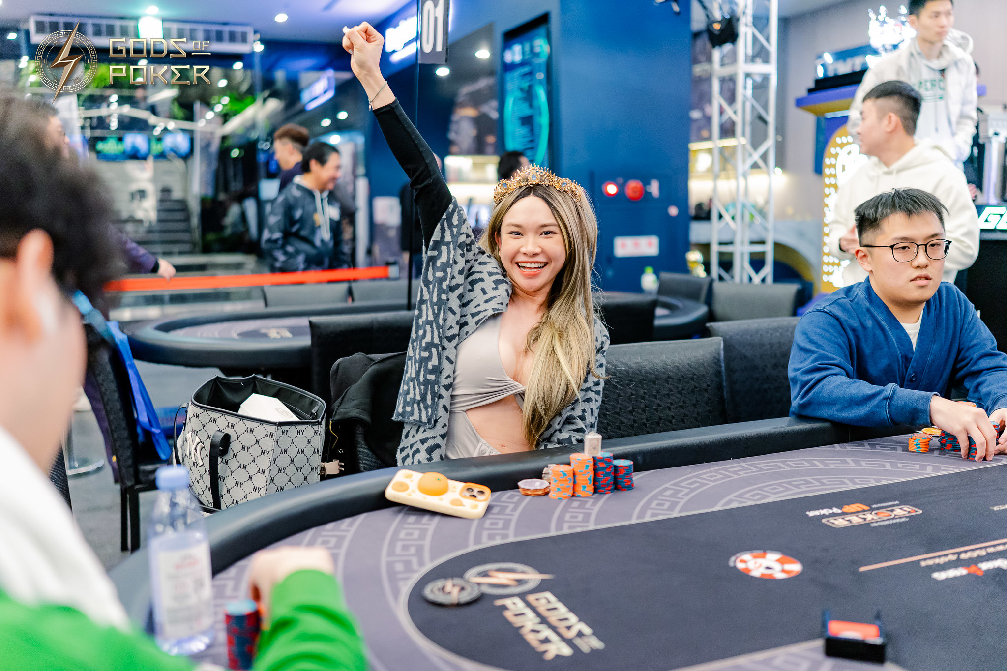 Smiling woman celebrates poker victory, raising arm with chips and cards on table.