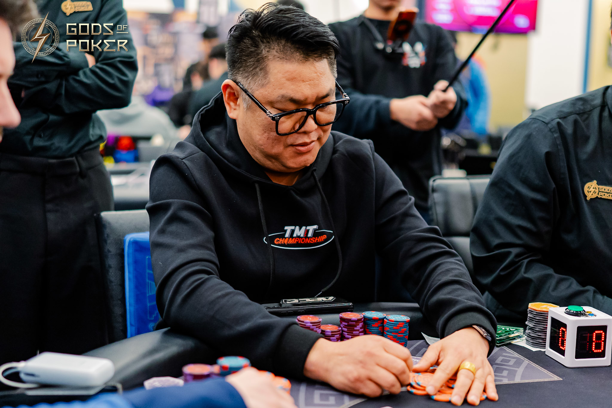 Man in glasses examining his poker cards at a table with chips.