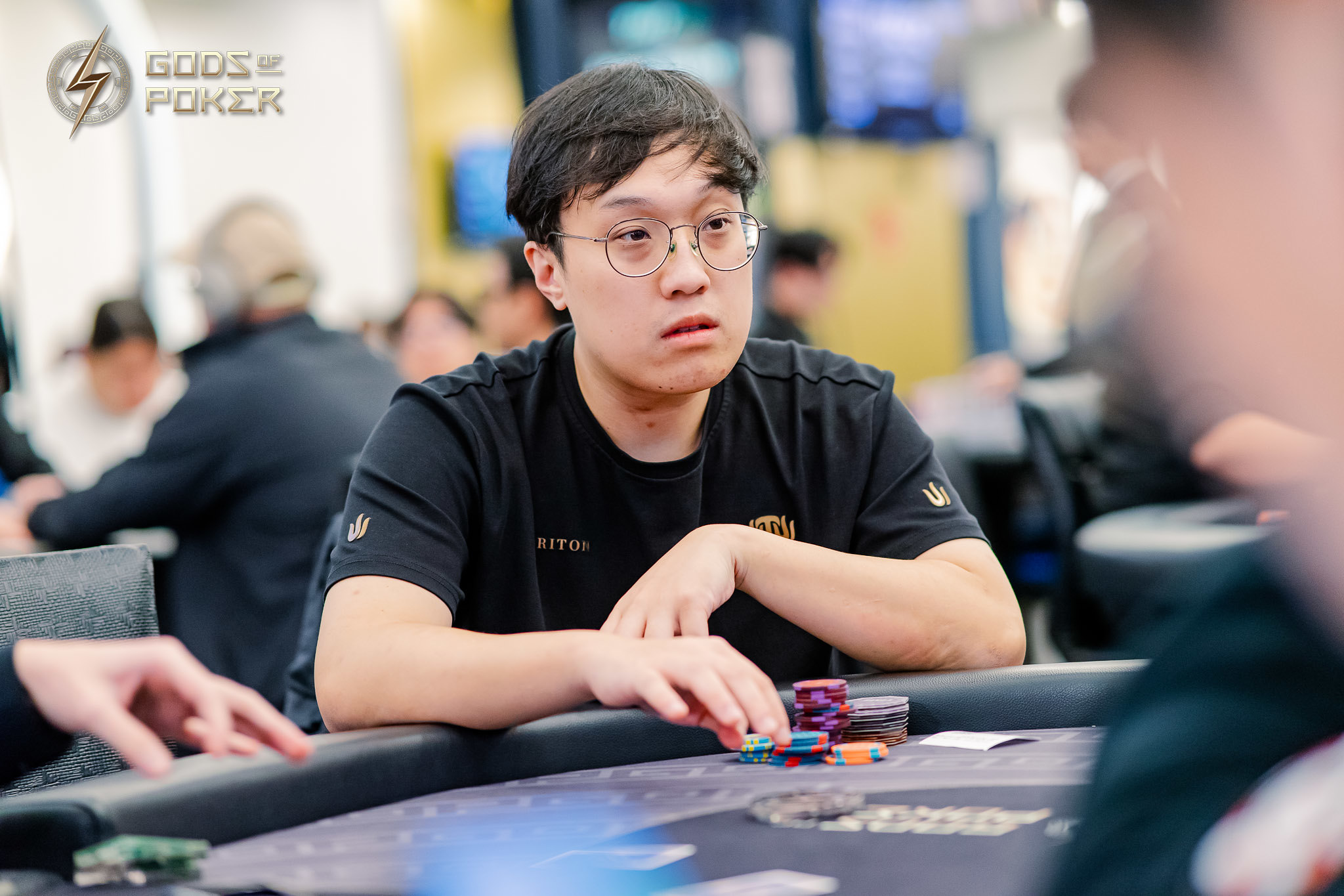 Young Asian man with glasses intently watching a poker game, chips on table.