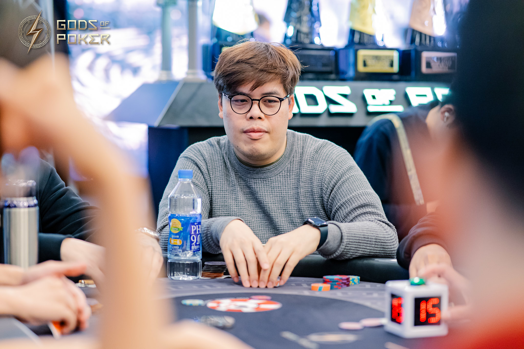 Man in glasses plays poker, serious expression, with chips and water.